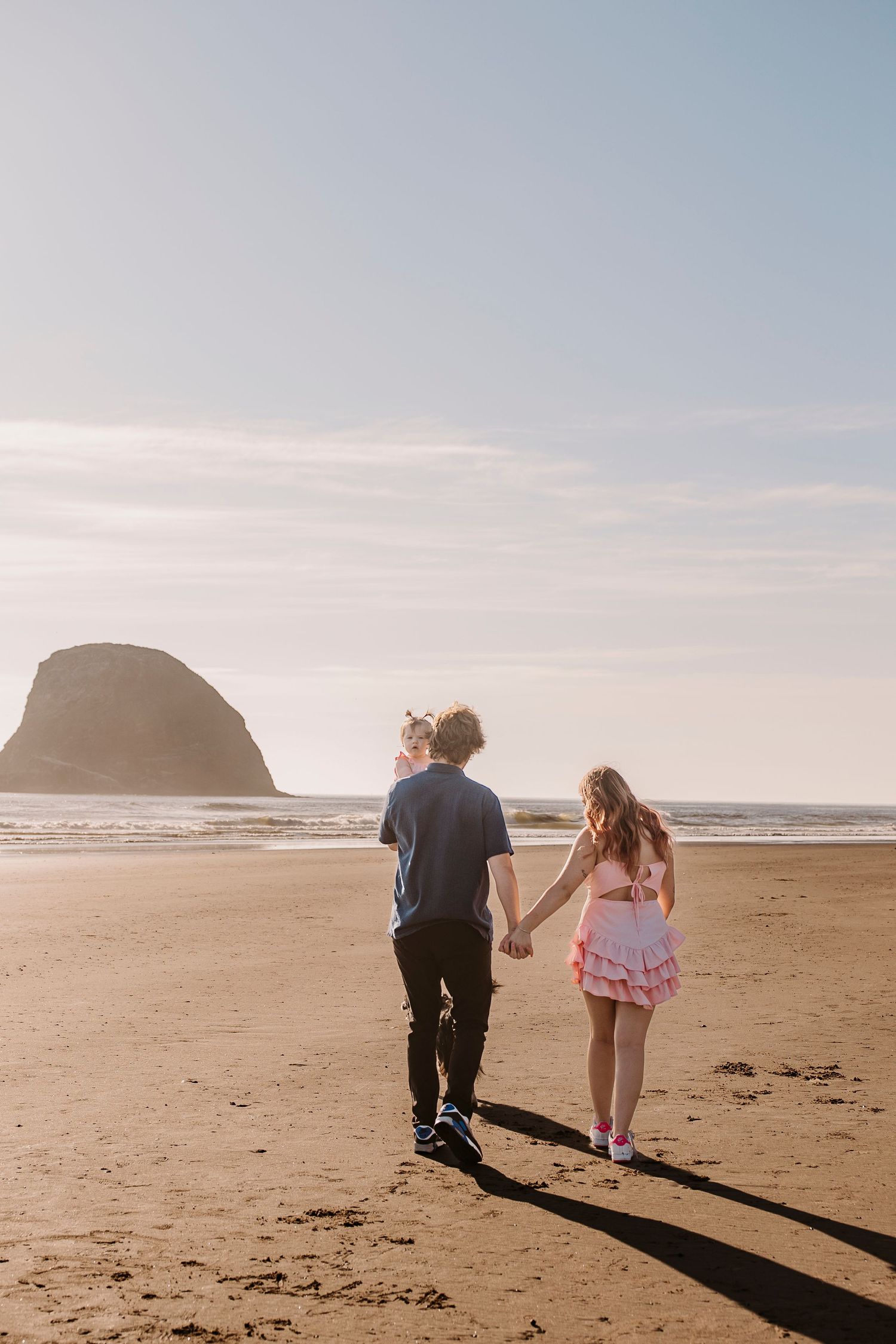 Family walking together on a sandy beach with cliffs and ocean views in the background.