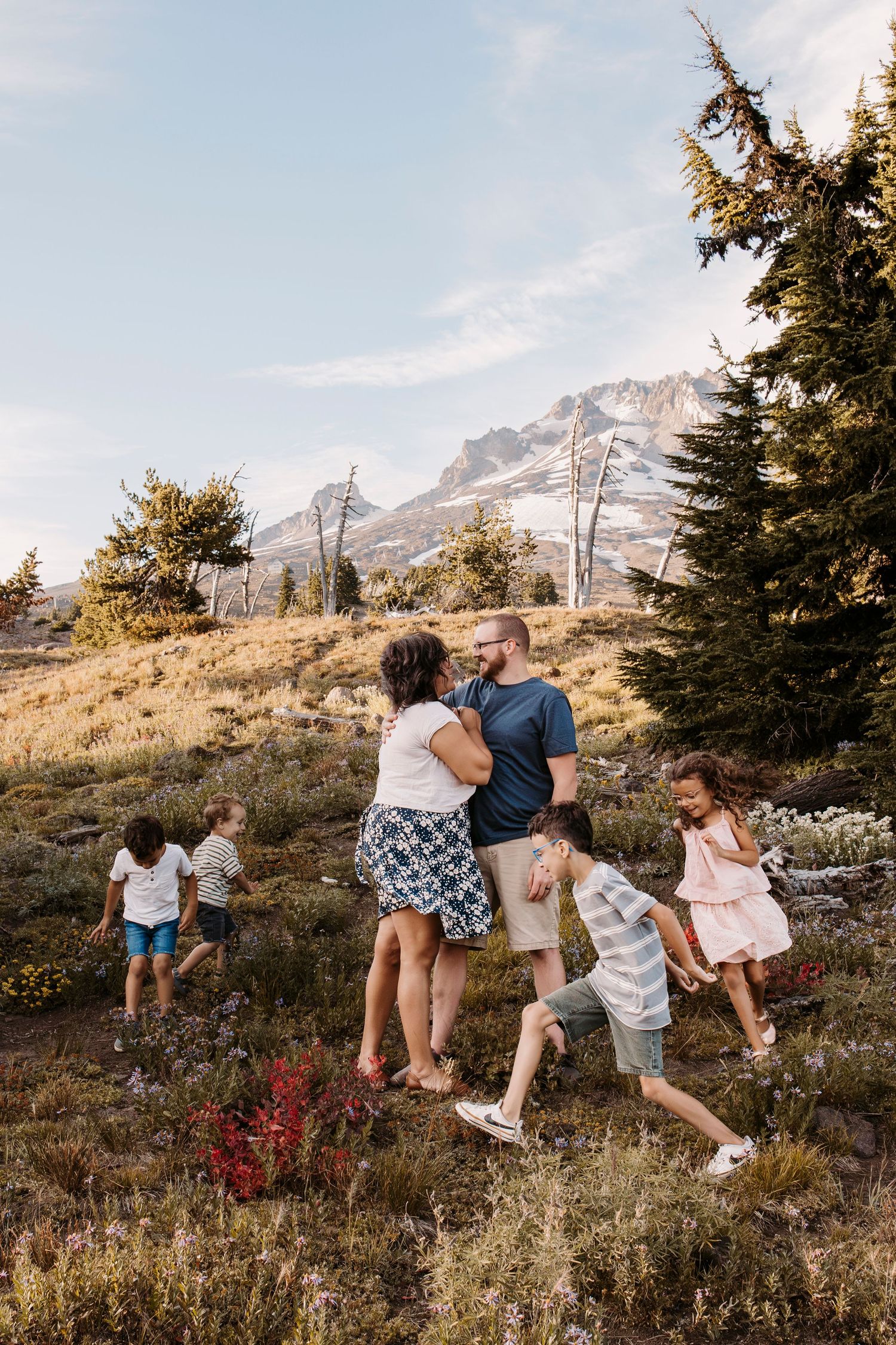 Family enjoying a hike together on a mountain trail with scenic snow-capped peaks in background.