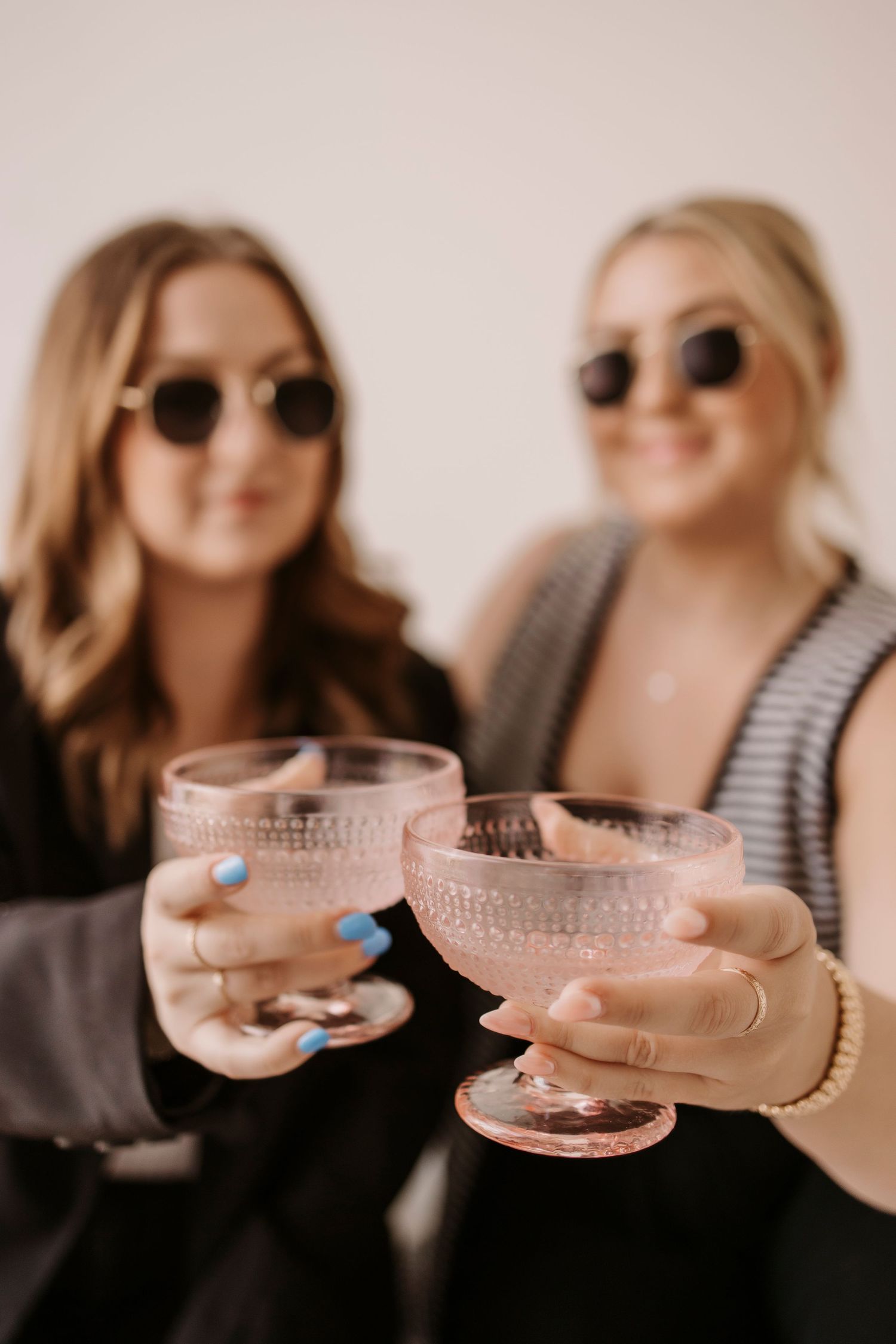 Friends in sunglasses toasting with pink champagne glasses in bright setting.