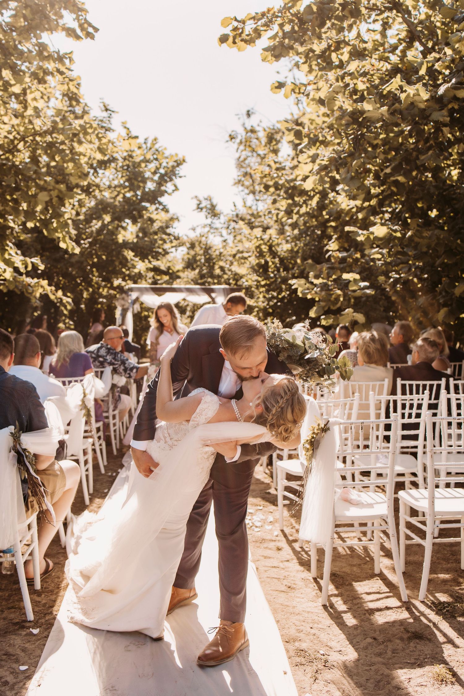 Romantic outdoor wedding ceremony with white chairs and couple sharing a special moment in golden sunlight.