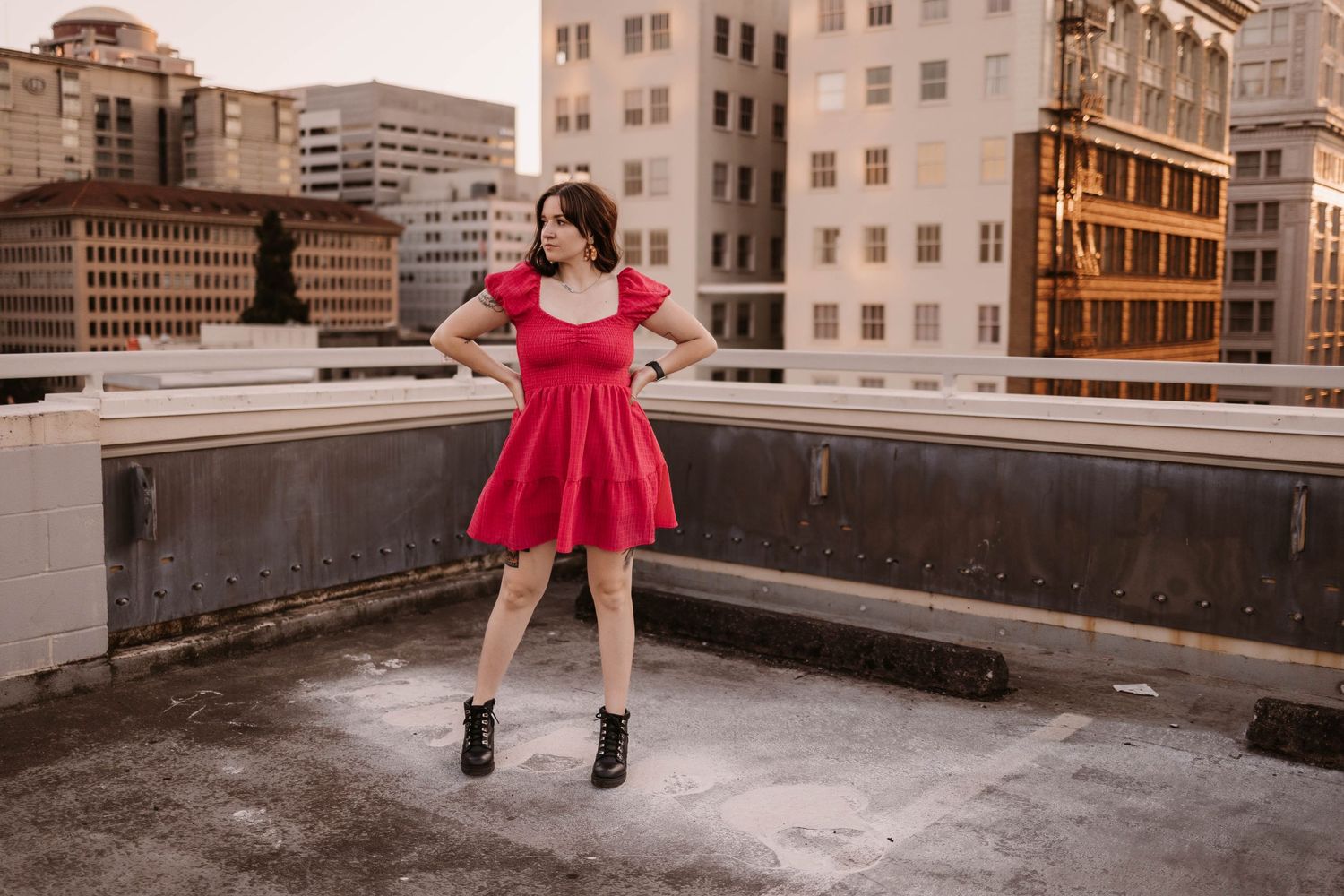 Dancing on a rooftop in a red dress with city buildings in the background.