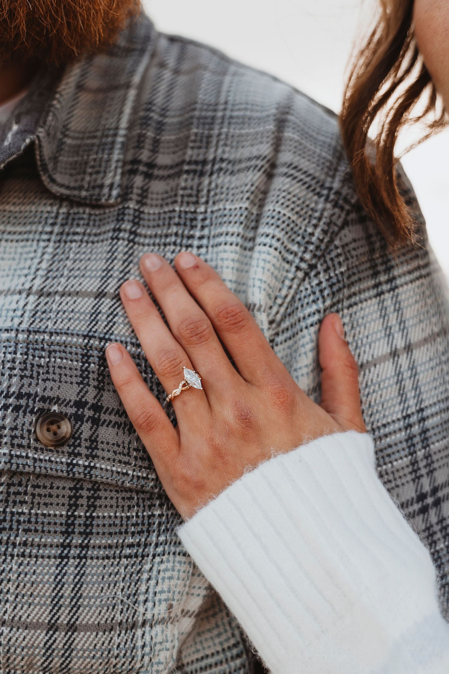 Close-up of engagement ring against plaid flannel jacket showing sparkly diamond.
