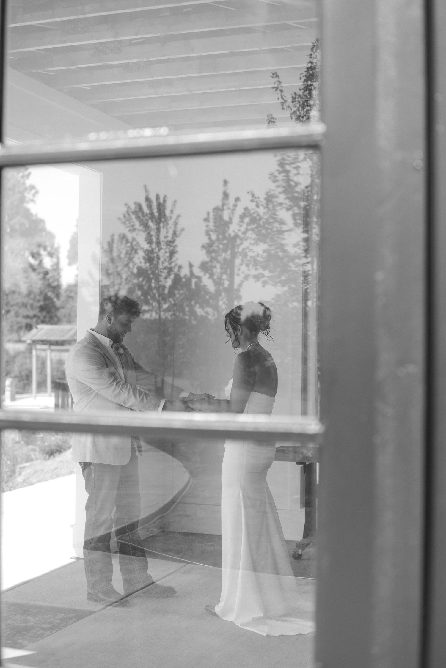 Wedding silhouettes captured through window reflections in black and white.