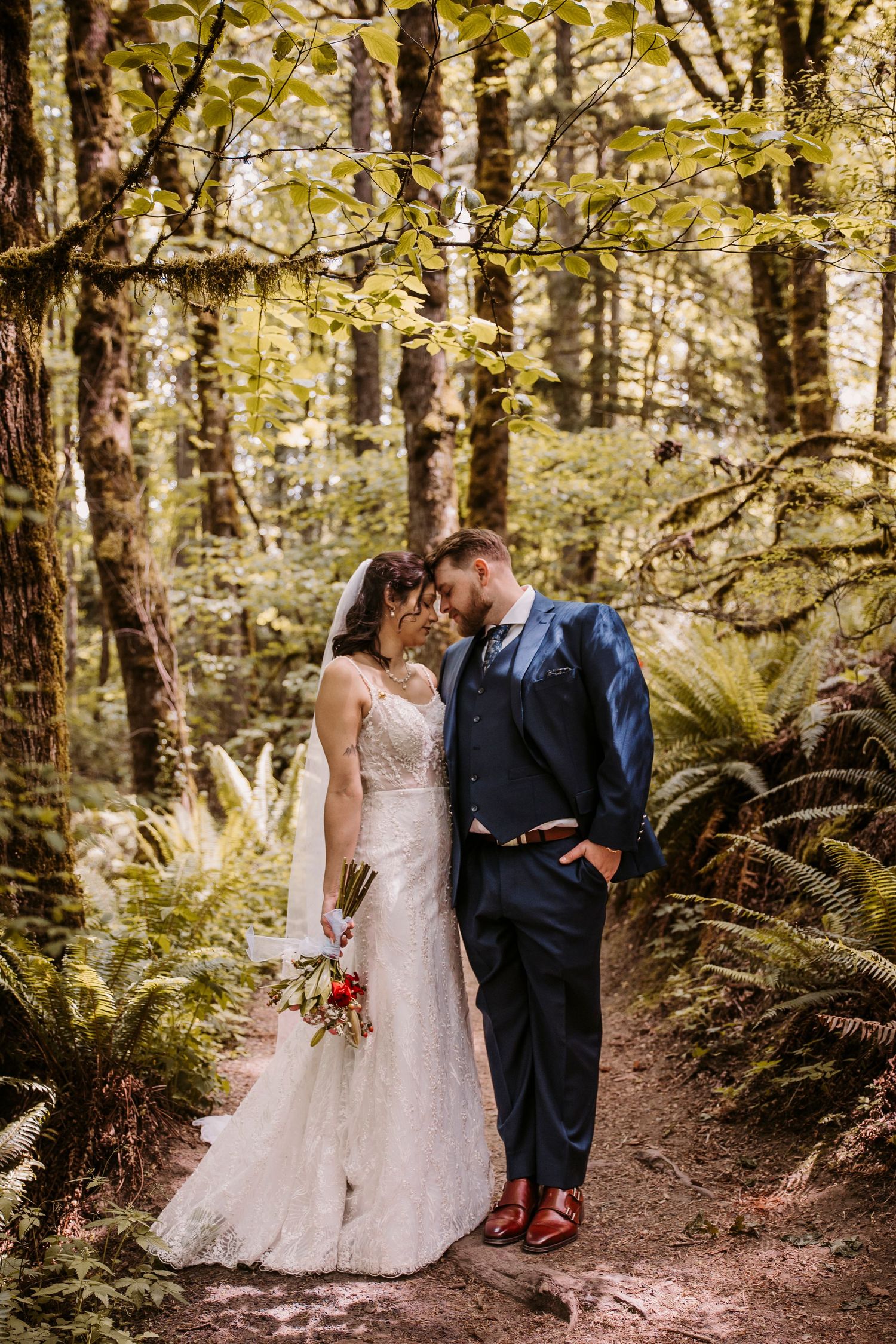 Wedding couple walking through lush forest path with ferns and autumn foliage.