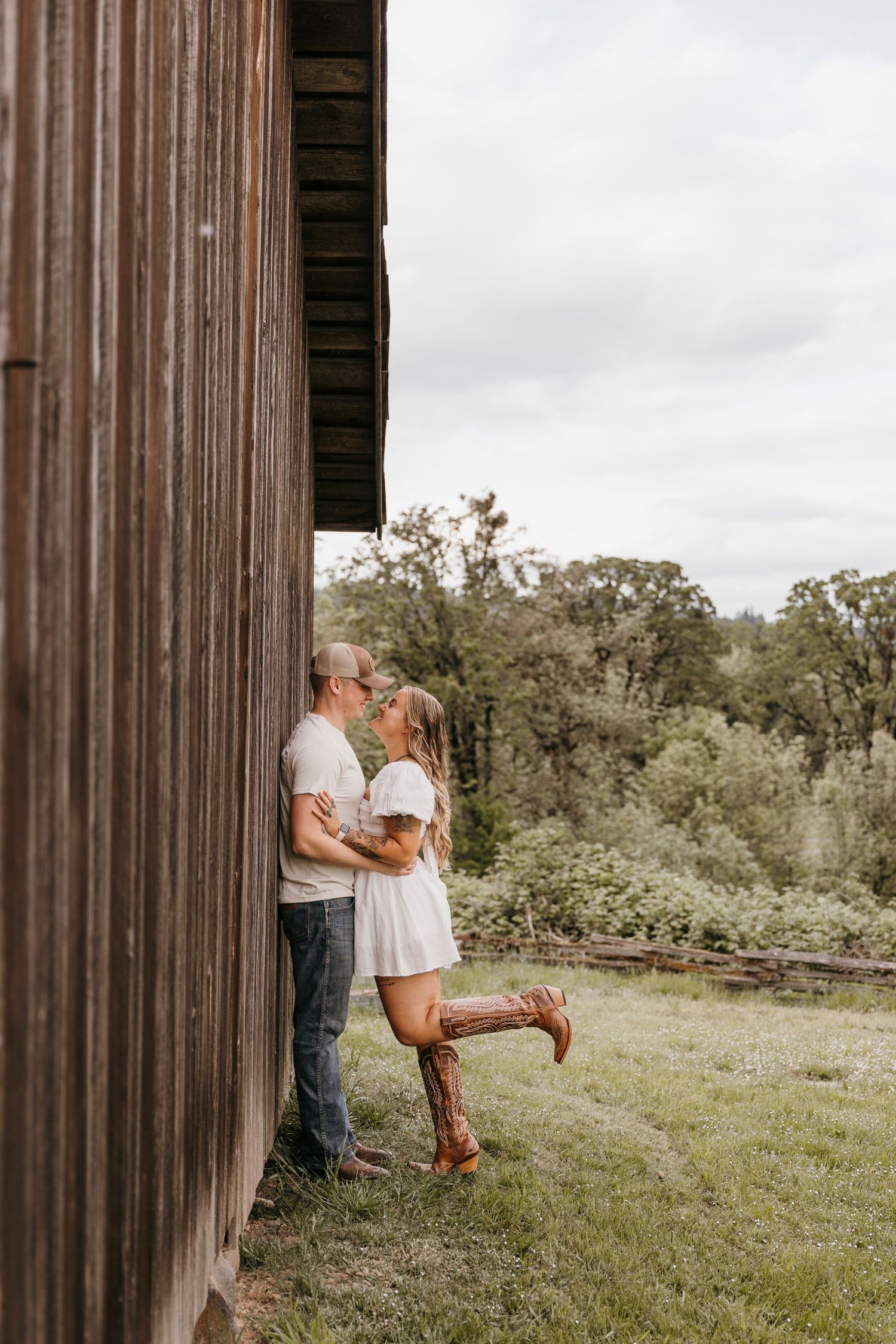 Couple shares intimate moments against rustic wooden barn in countryside setting.