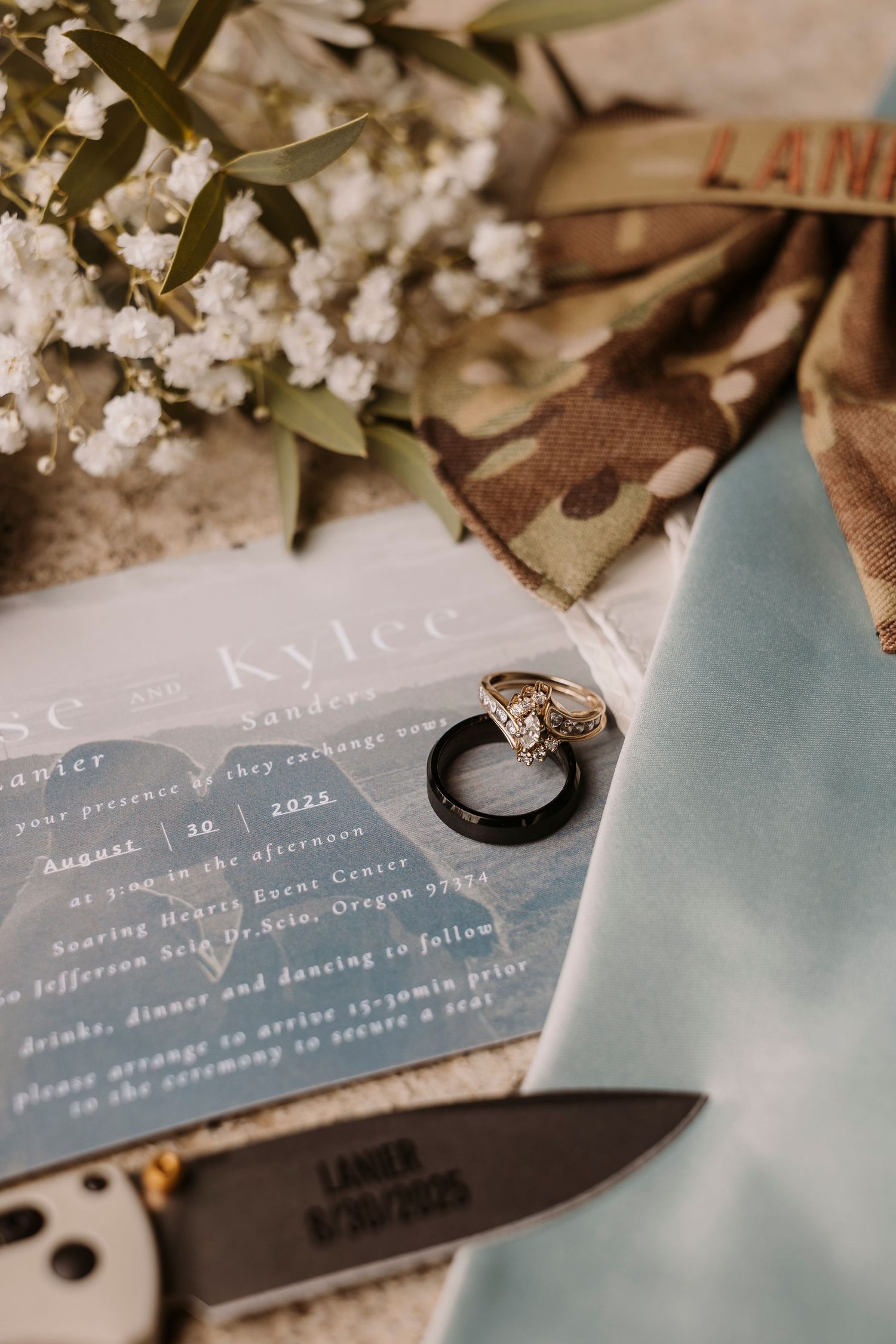 Wedding invitation suite with white cherry blossoms and engagement rings on blue paper.