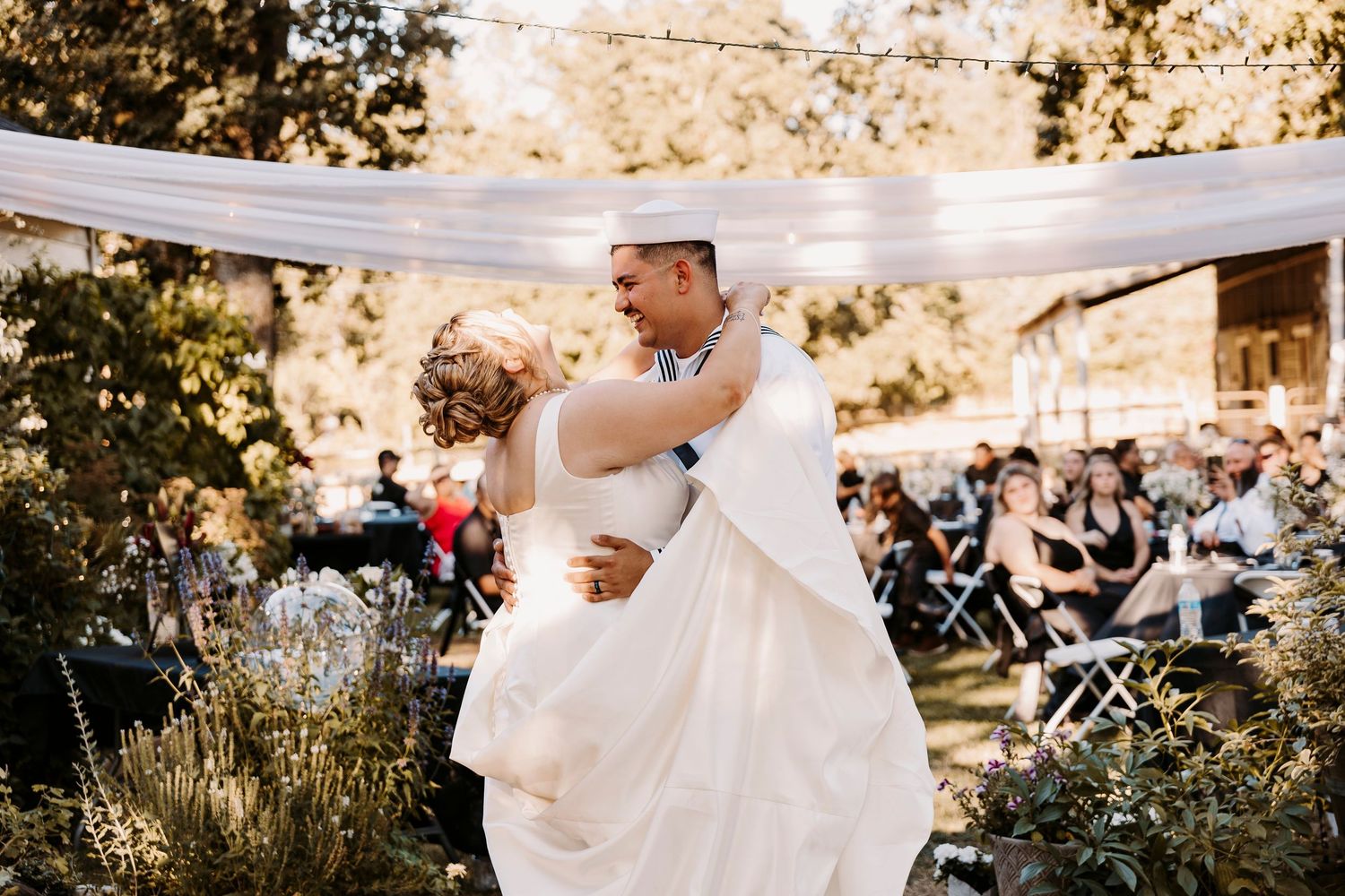 A couple shares their first dance under a white fabric canopy at an outdoor wedding reception.