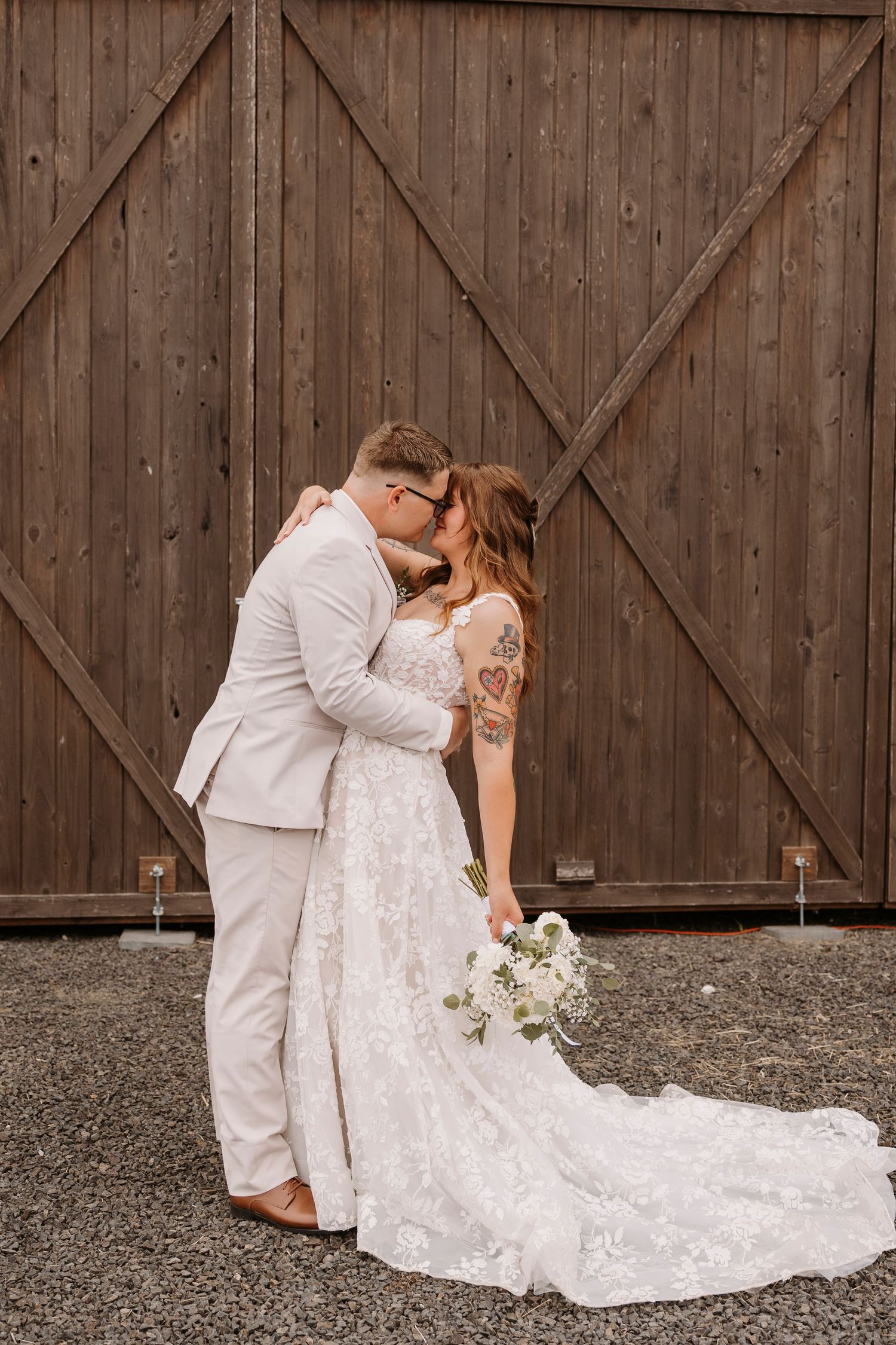 A romantic wedding portrait against a rustic barn door features a lace dress with flowing train.