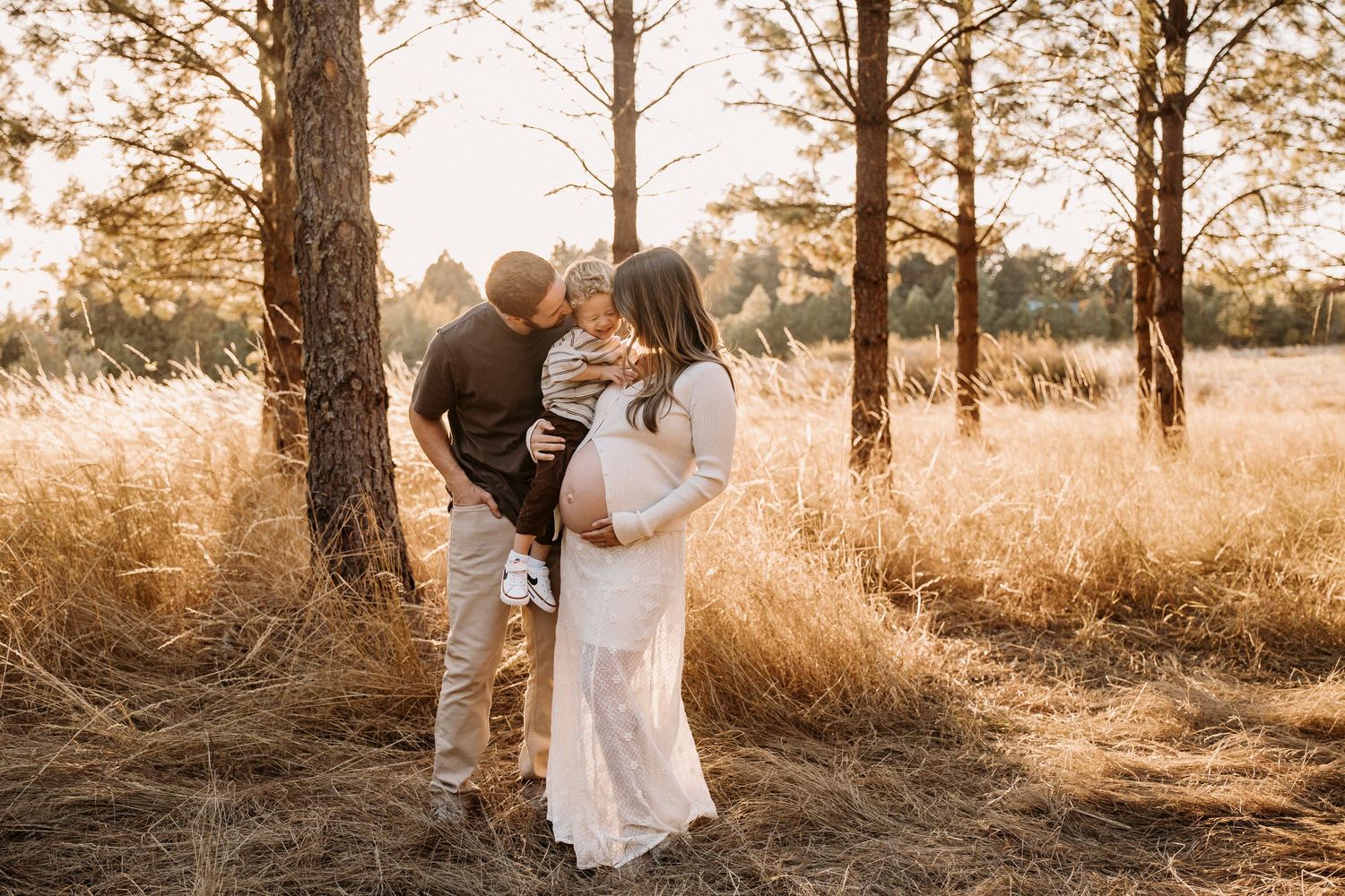 Couple embracing in a sun-drenched forest with golden light filtering through trees.