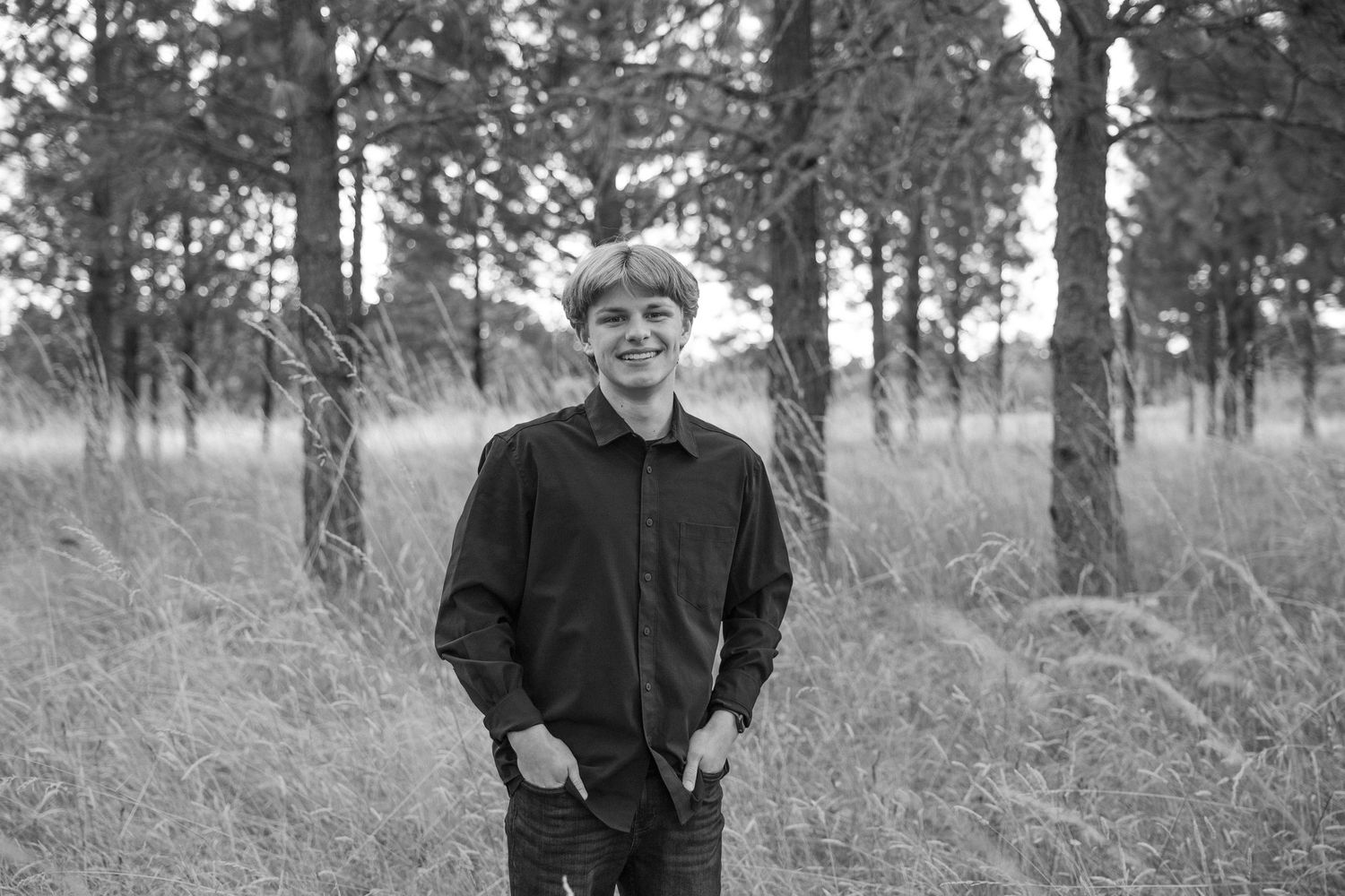Black and white portrait in wooded setting with pine trees in background.