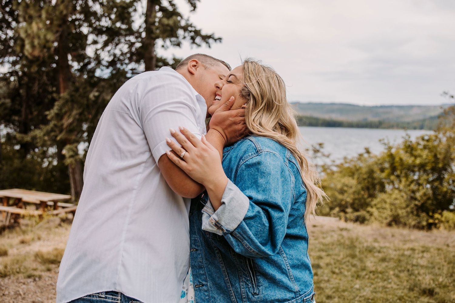 A couple shares an intimate moment overlooking a scenic lake and mountain landscape.