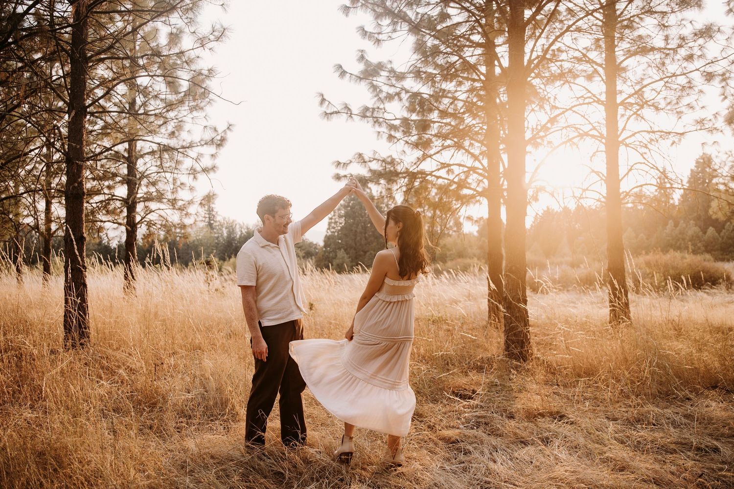 Romantic sunset photos in a golden field with pine trees creating a dreamy backdrop.
