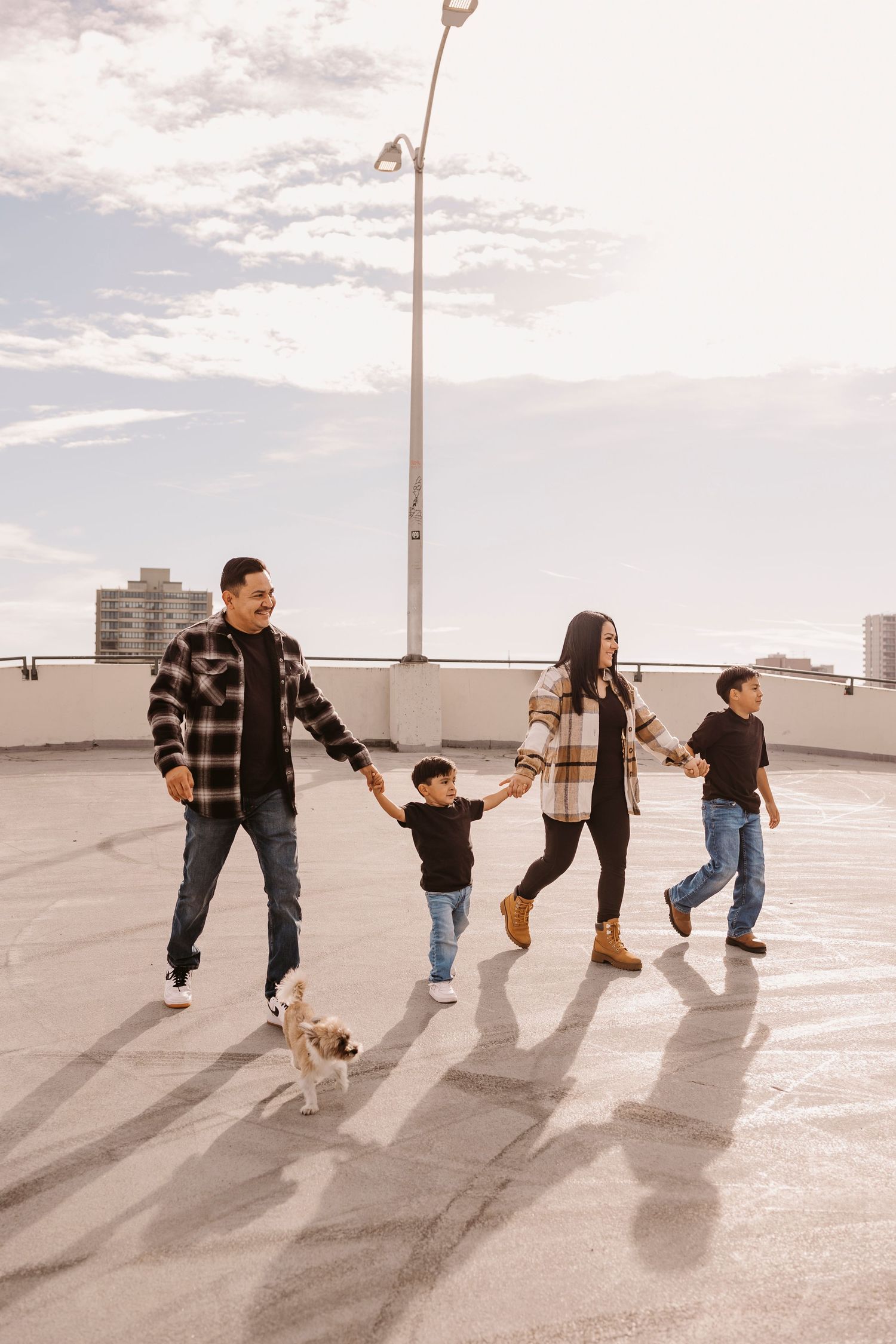 A family holds hands while walking in a line casting long shadows on a concrete surface.