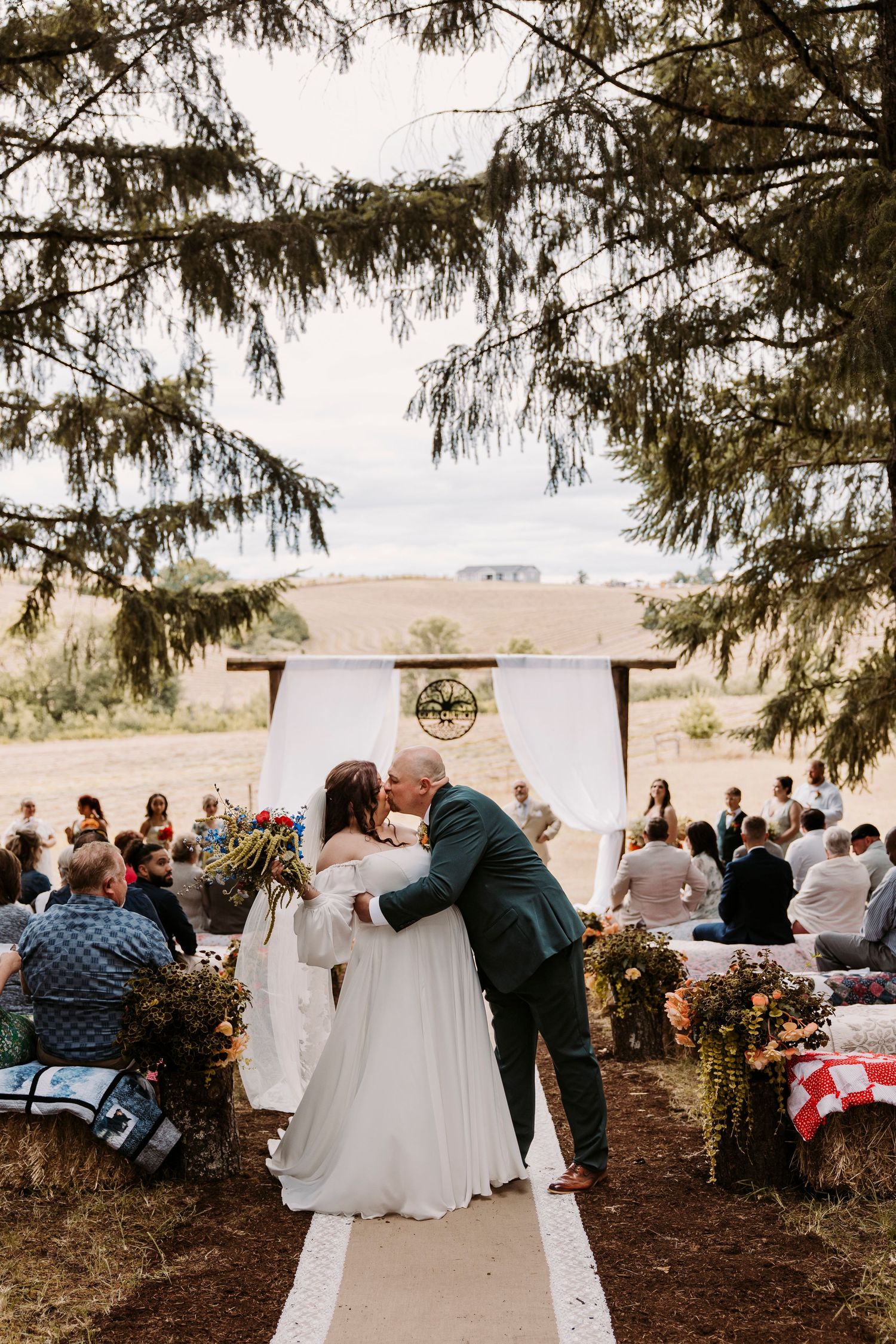 Outdoor wedding ceremony setup with white chairs and decor under evergreen trees.
