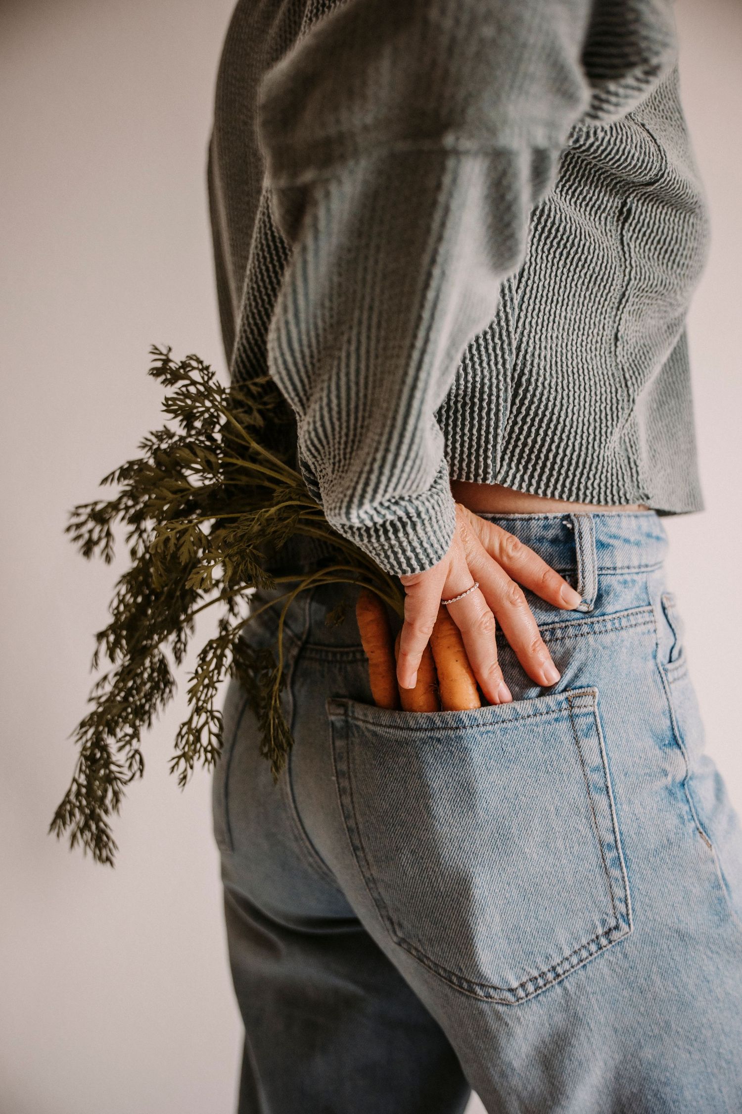 Close-up of jeans pocket with greenery sticking out against neutral background.