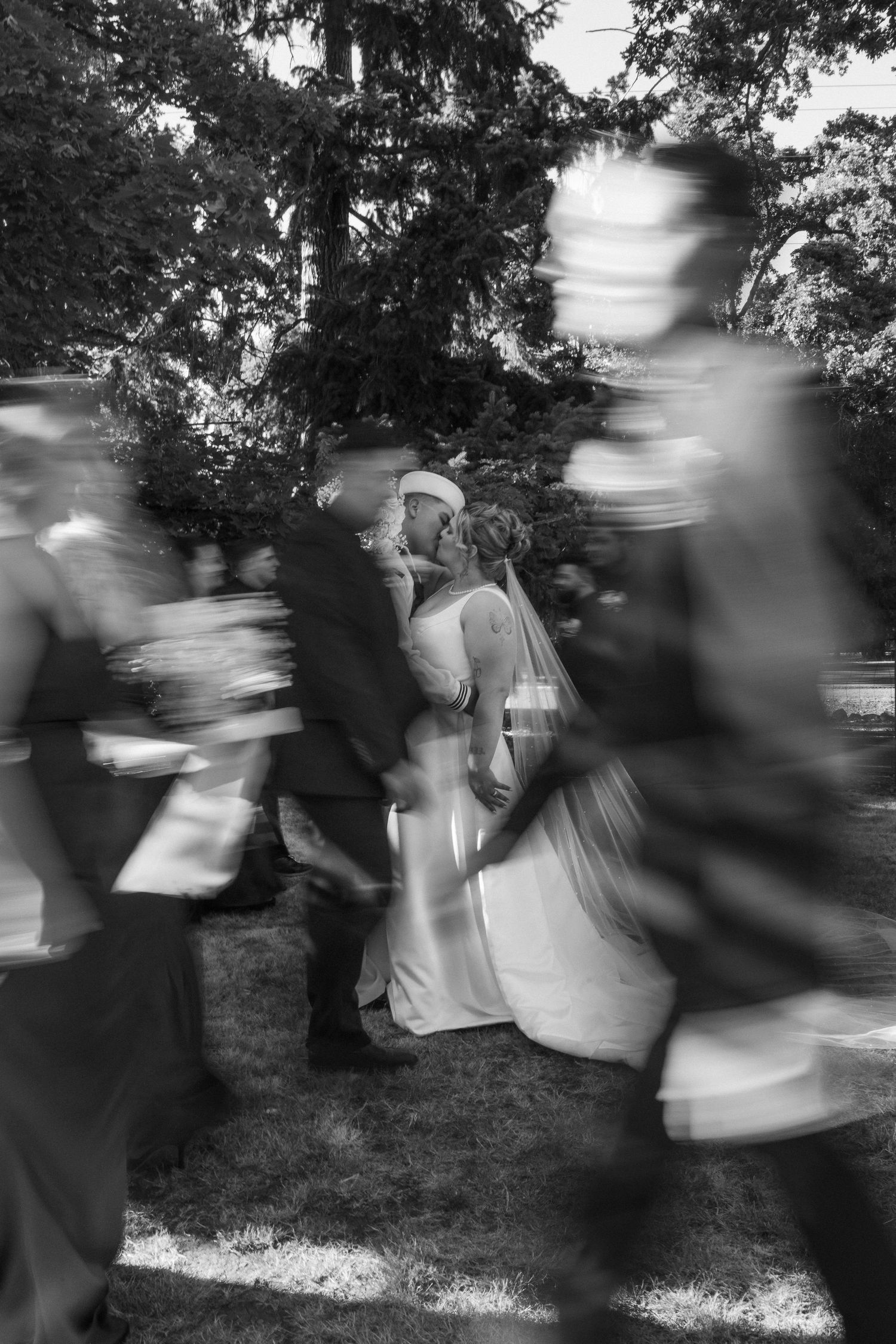 Motion-blurred black and white photo of dancing figures in an outdoor setting.