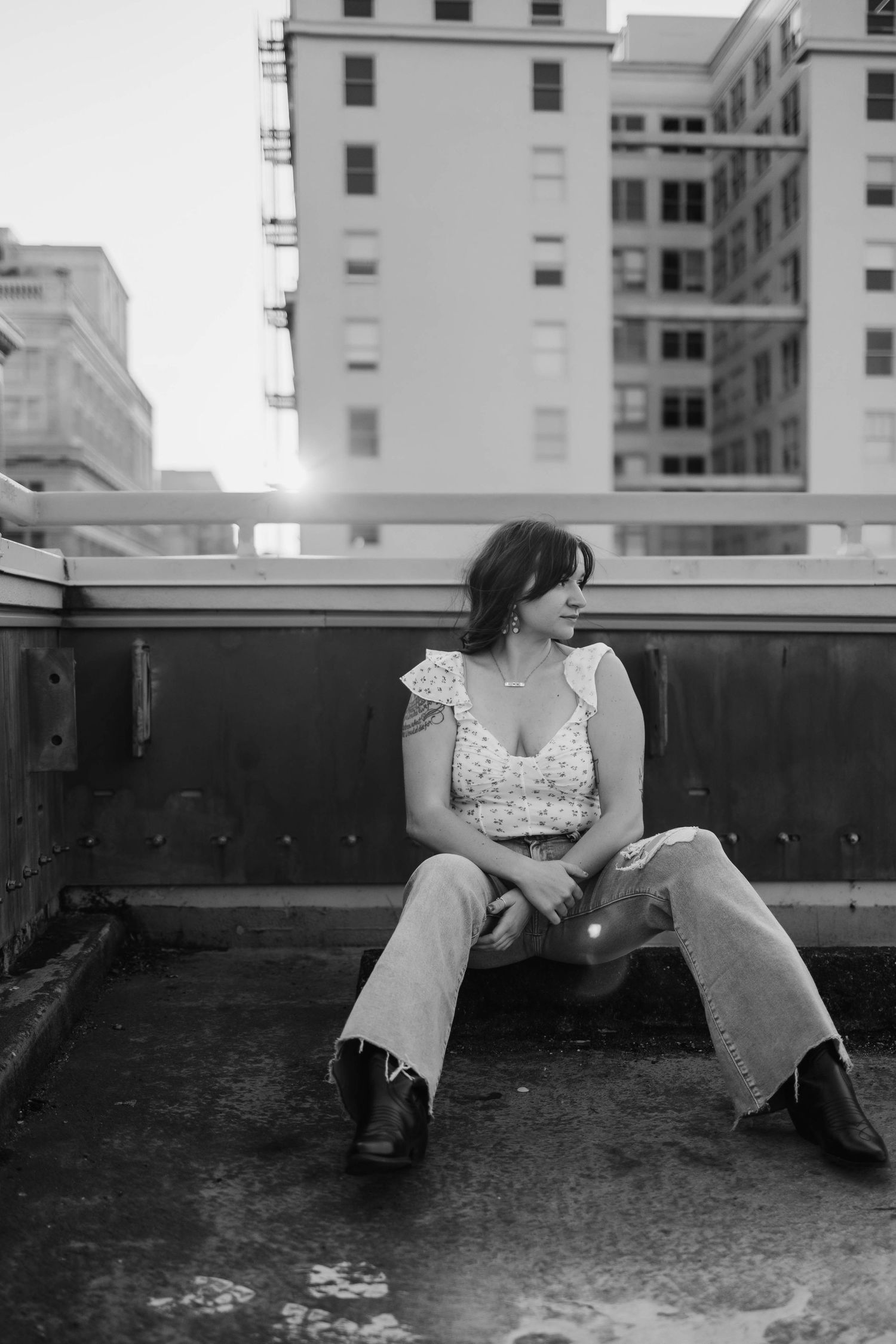 Black and white urban portrait on rooftop with city buildings in background.