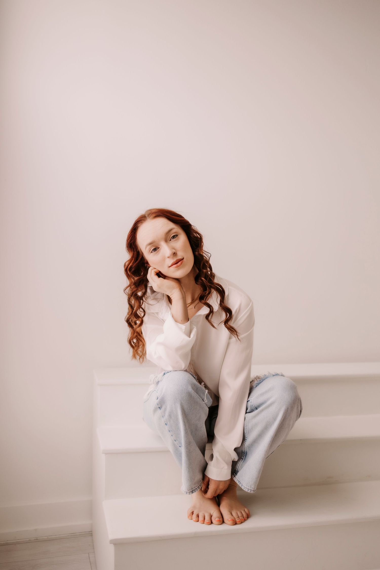 Minimalist portrait on white stairs showing casual comfort in neutral toned clothing.