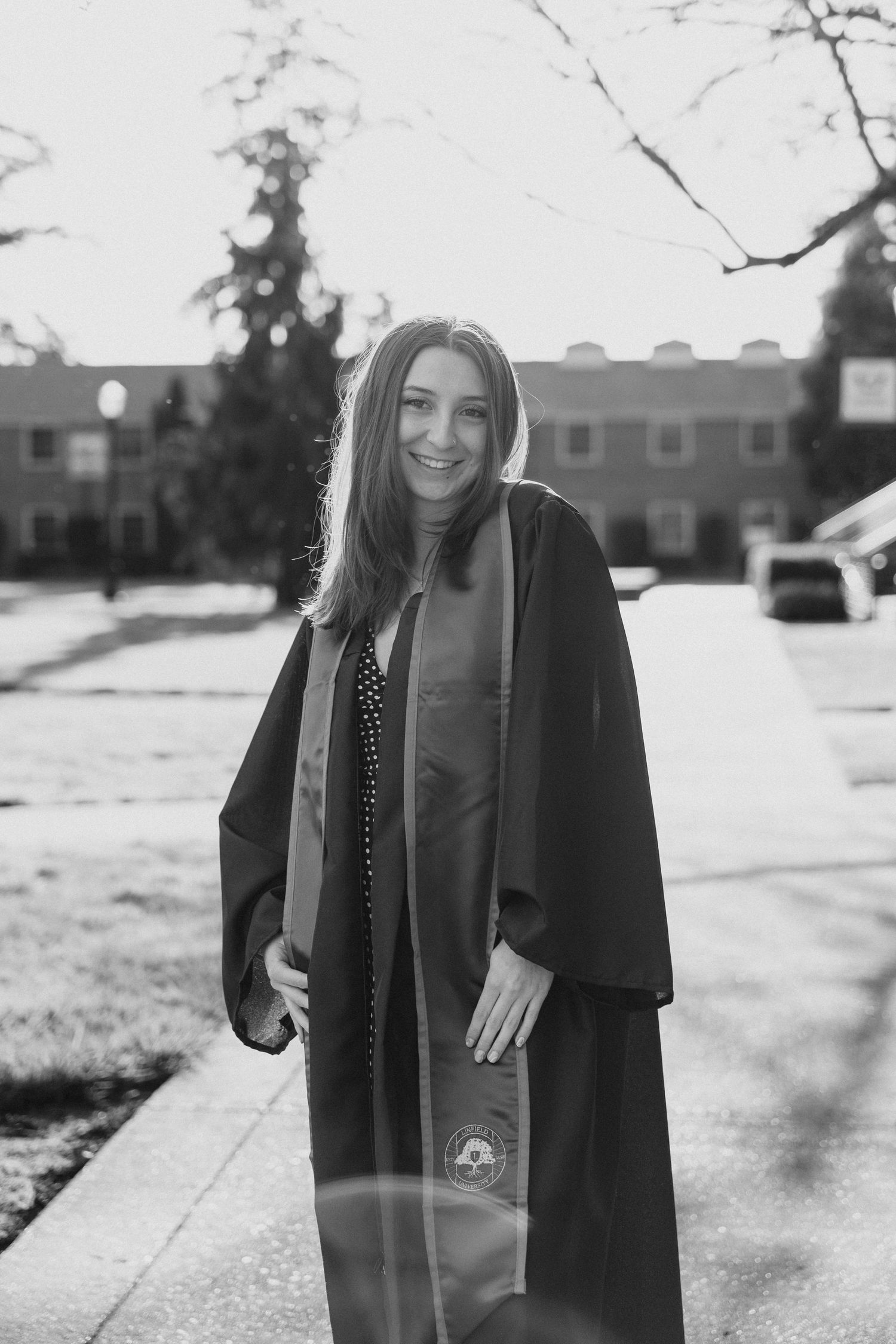 Black and white graduation portrait on campus sidewalk with academic buildings in background.