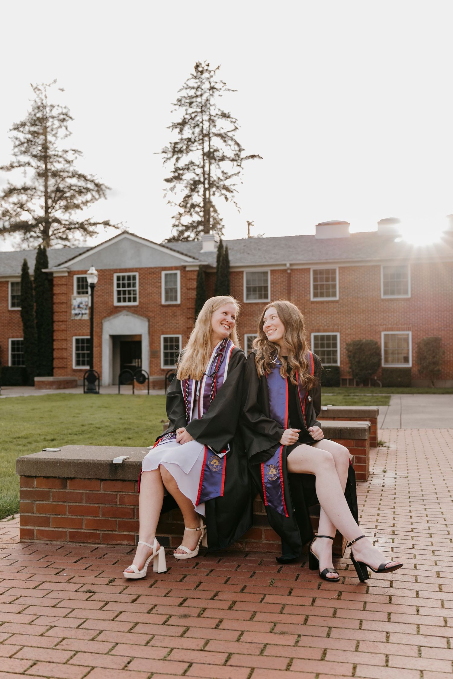 Two graduates sitting on brick wall during sunset photoshoot.