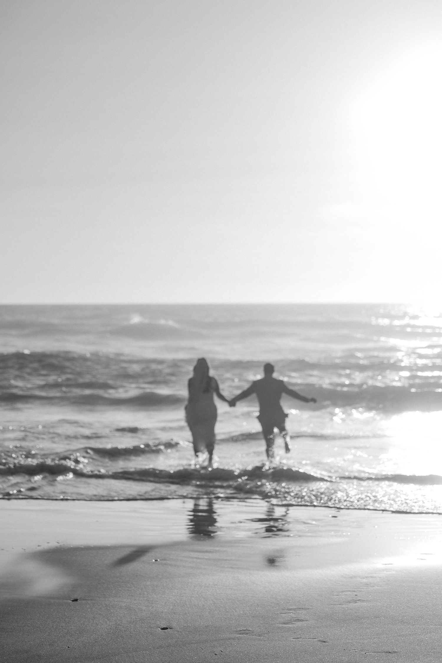 Silhouetted couple walking along misty beach shoreline at sunset.