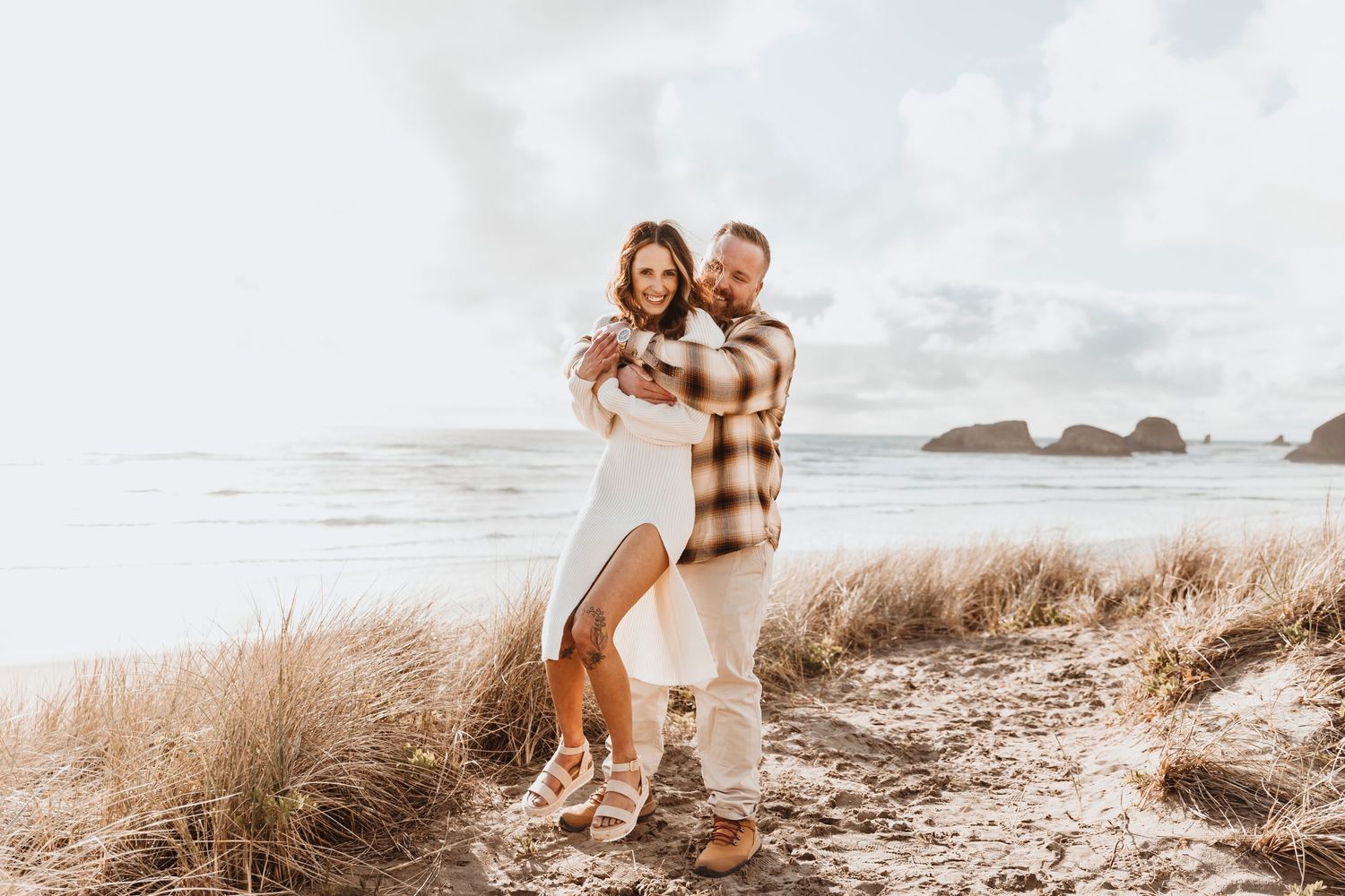 Romantic beach engagement photos at sunset with coastal rocks in background.
