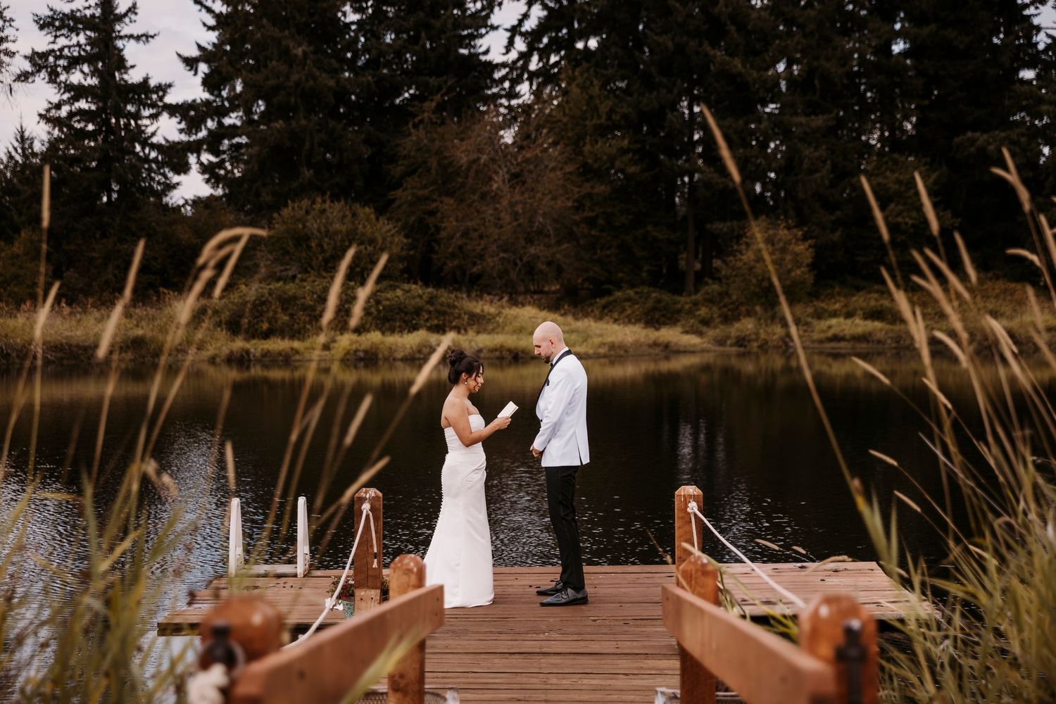 Rustic wooden dock wedding ceremony location surrounded by tall grass and evergreen trees.