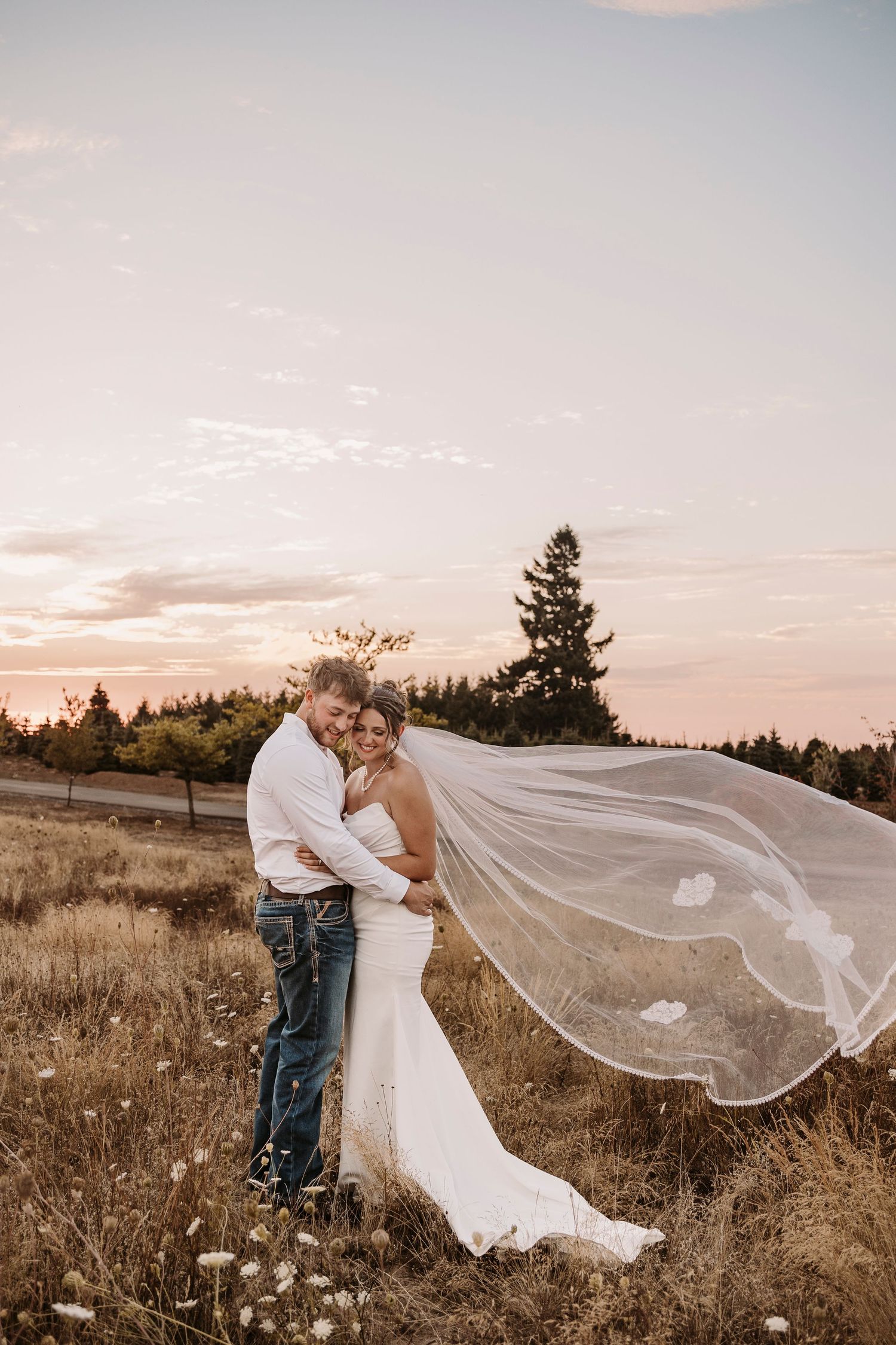 Romantic sunset portrait with flowing veil in a rustic field setting.
