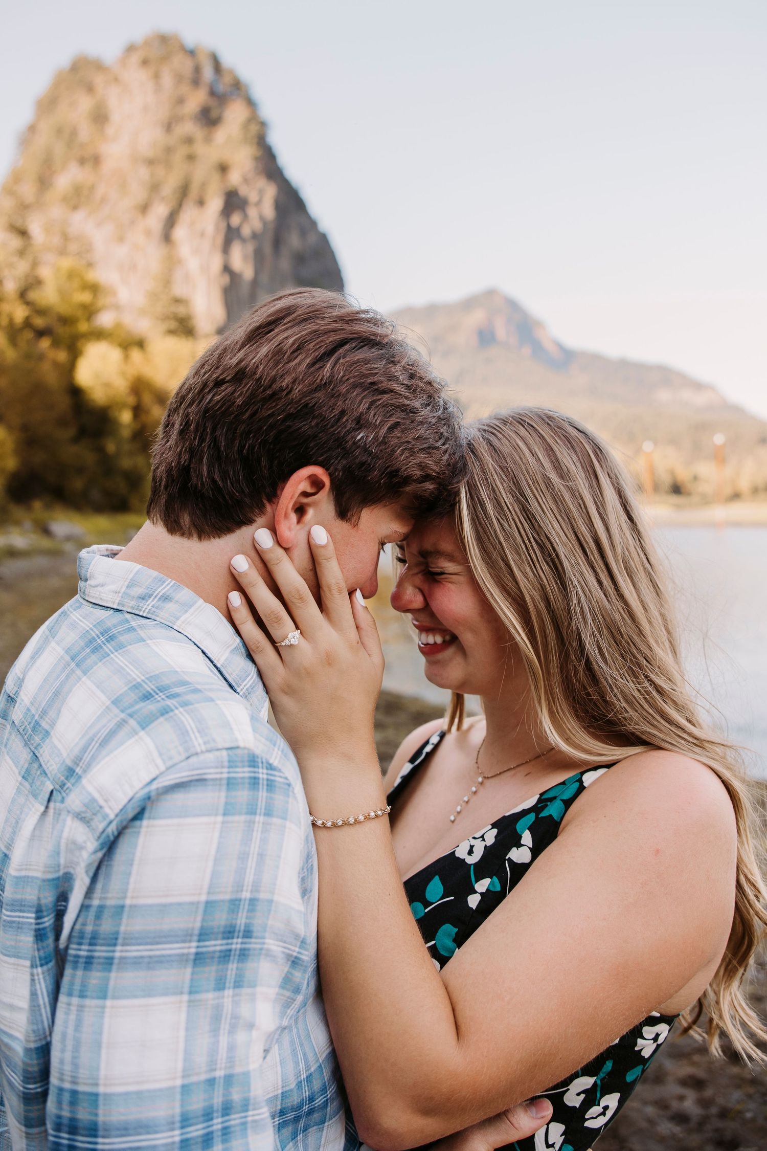 Couple shares tender moments by a scenic lake with mountains in background.