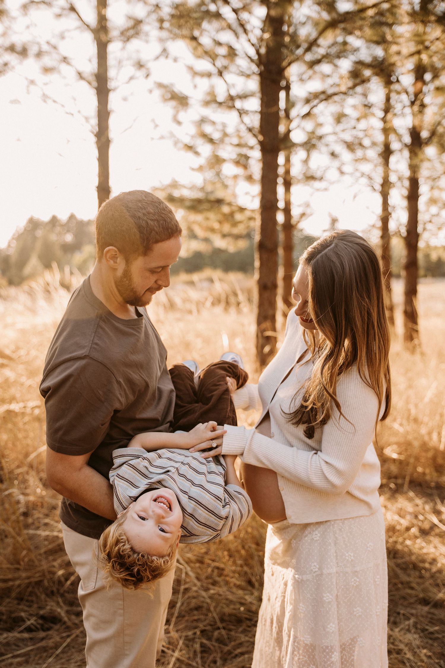 Family maternity photoshoot in a golden sunlit forest setting.