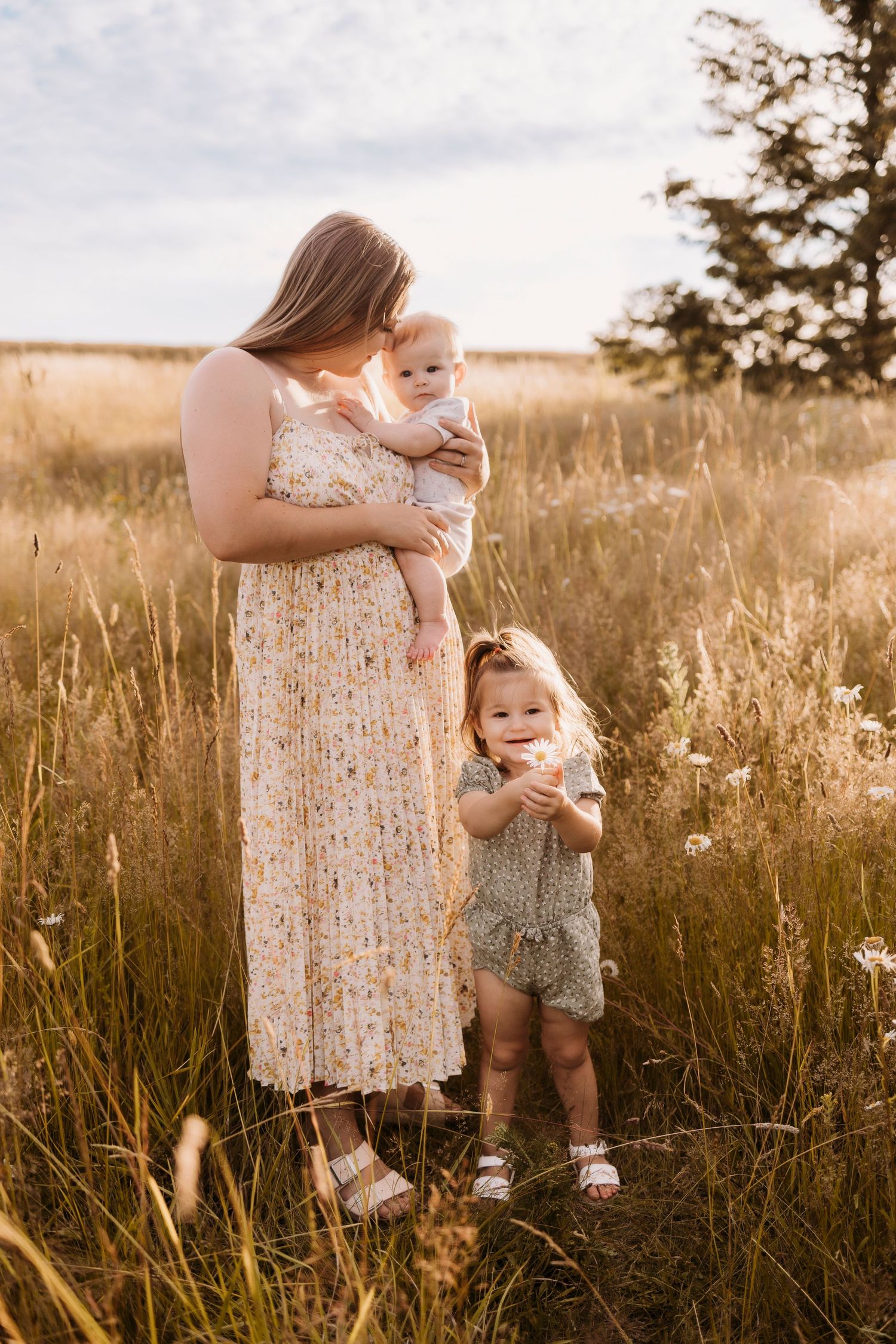 Mother and children standing in tall grass field during golden hour.