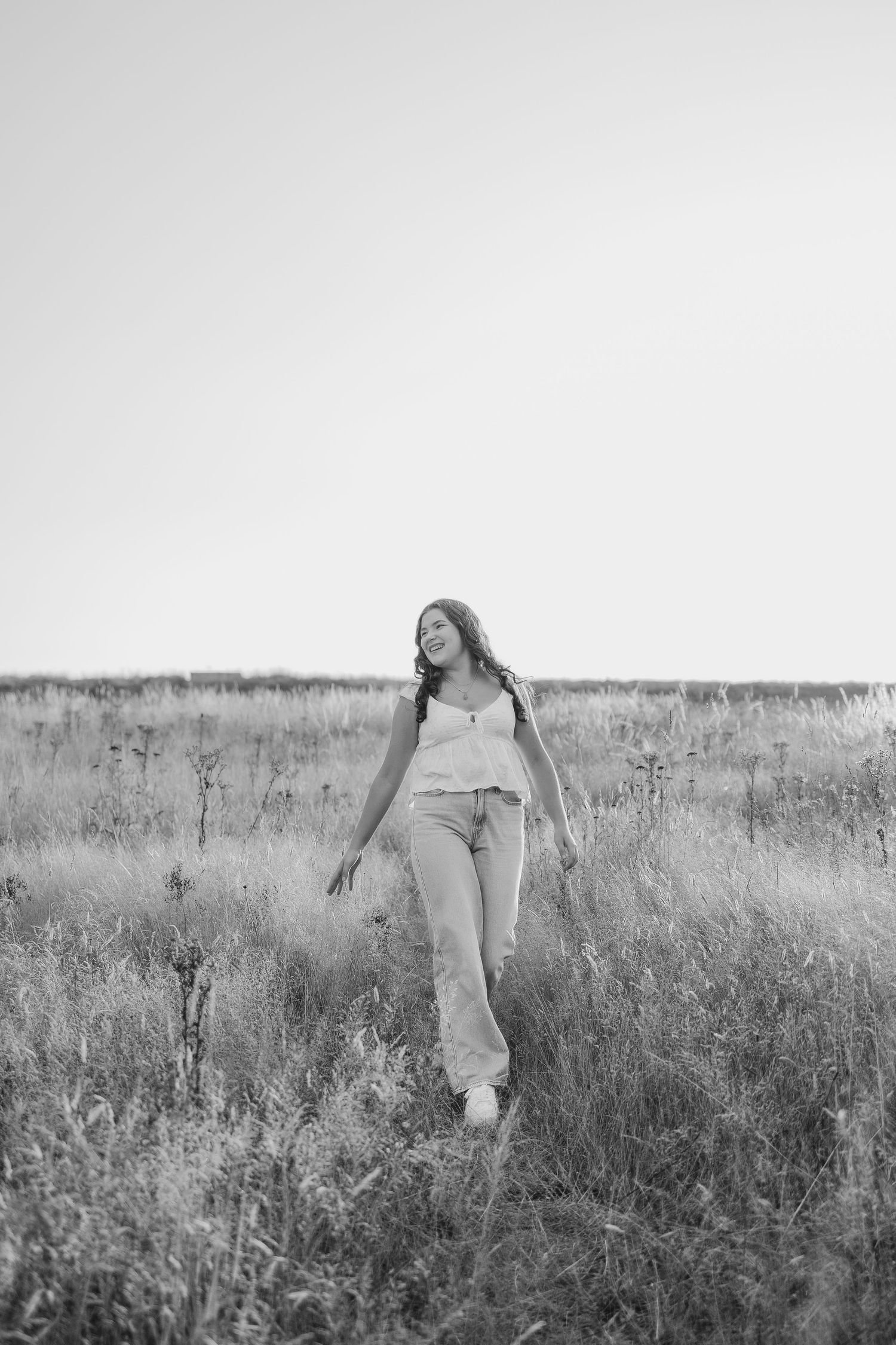 Black and white portrait of someone walking through tall grass in a dreamy field setting.