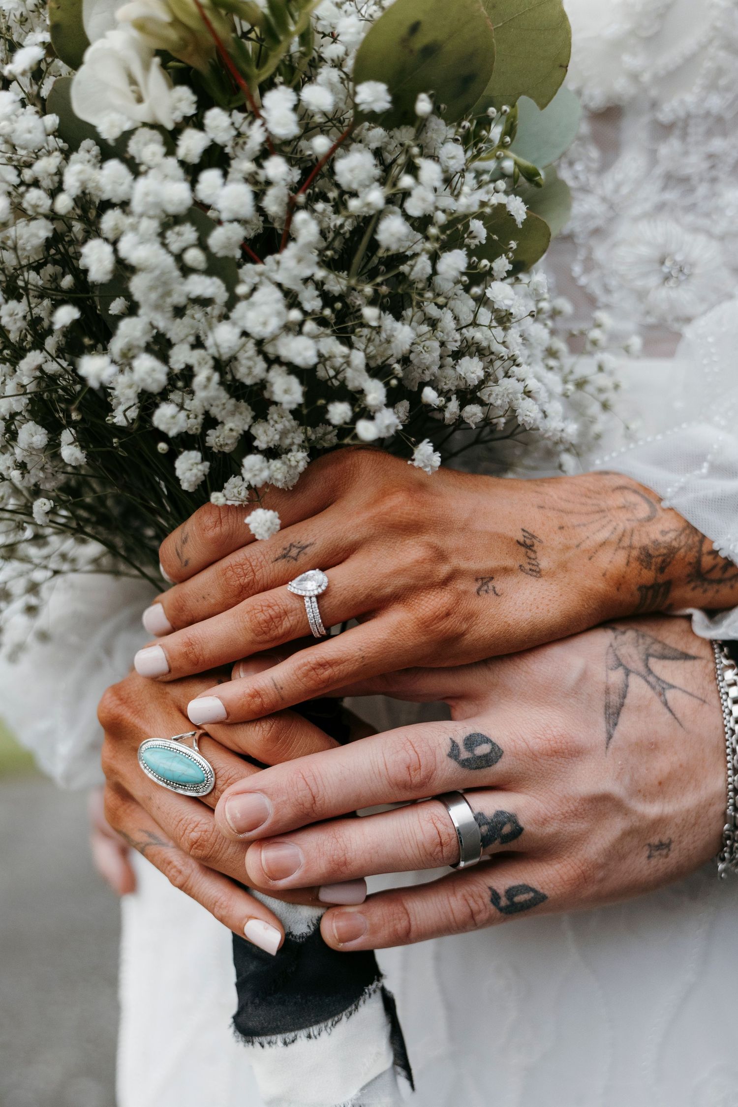 Close-up of tattooed hands with wedding rings holding a white floral bouquet.