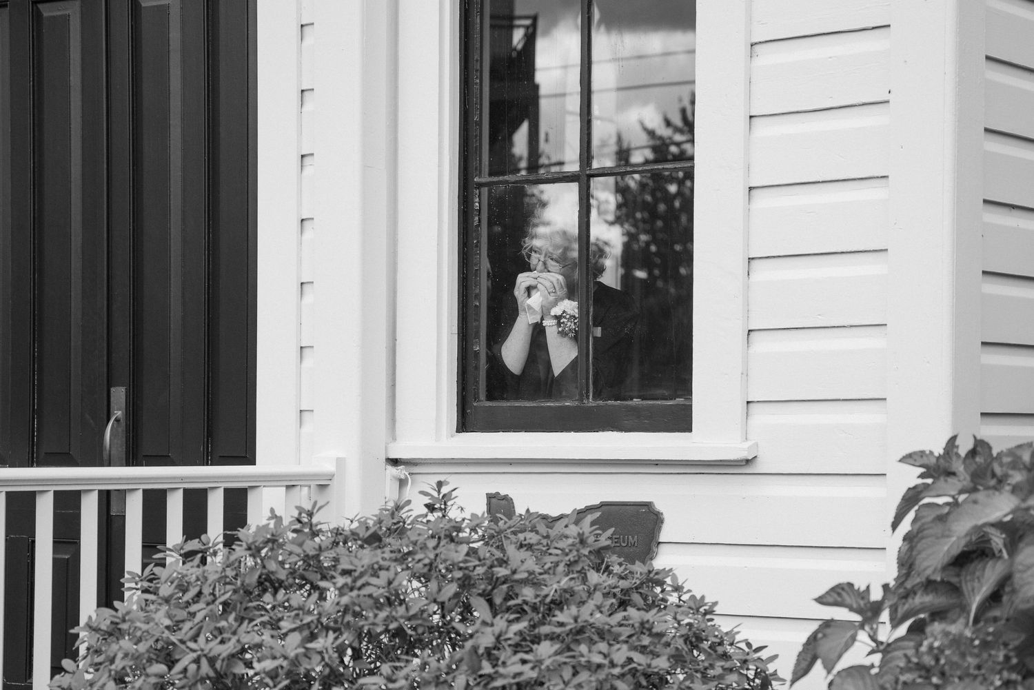 A candid view through a window shows a figure peeking out from inside a white building.