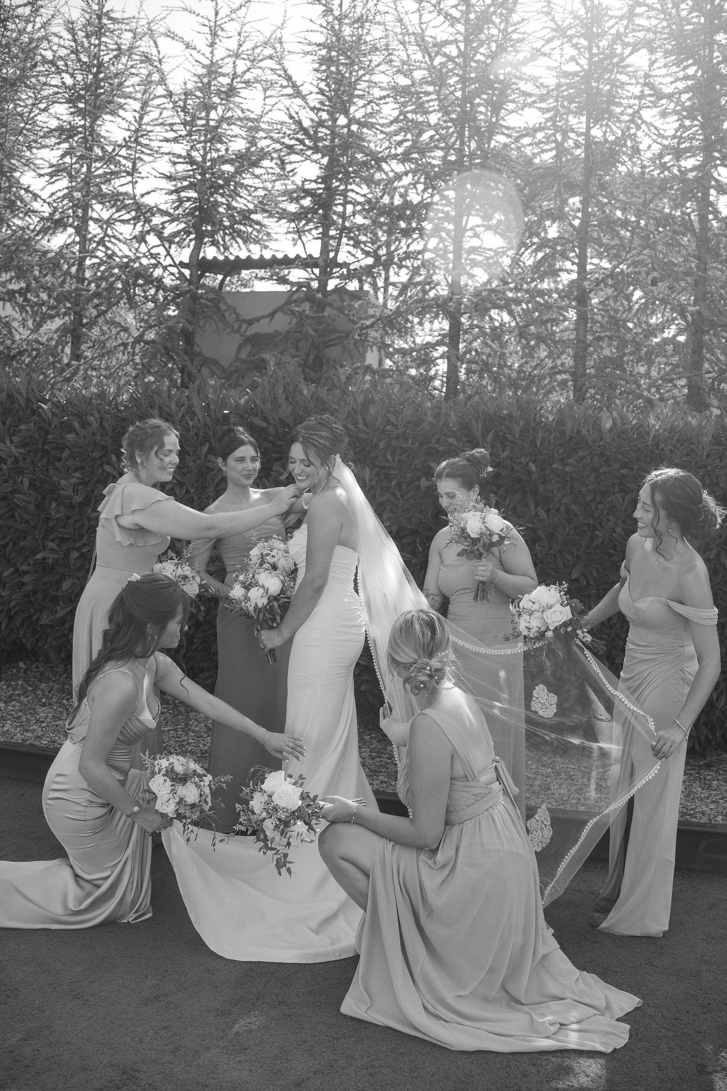 Black and white photo of bridesmaids in matching dresses arranging the bride's gown.