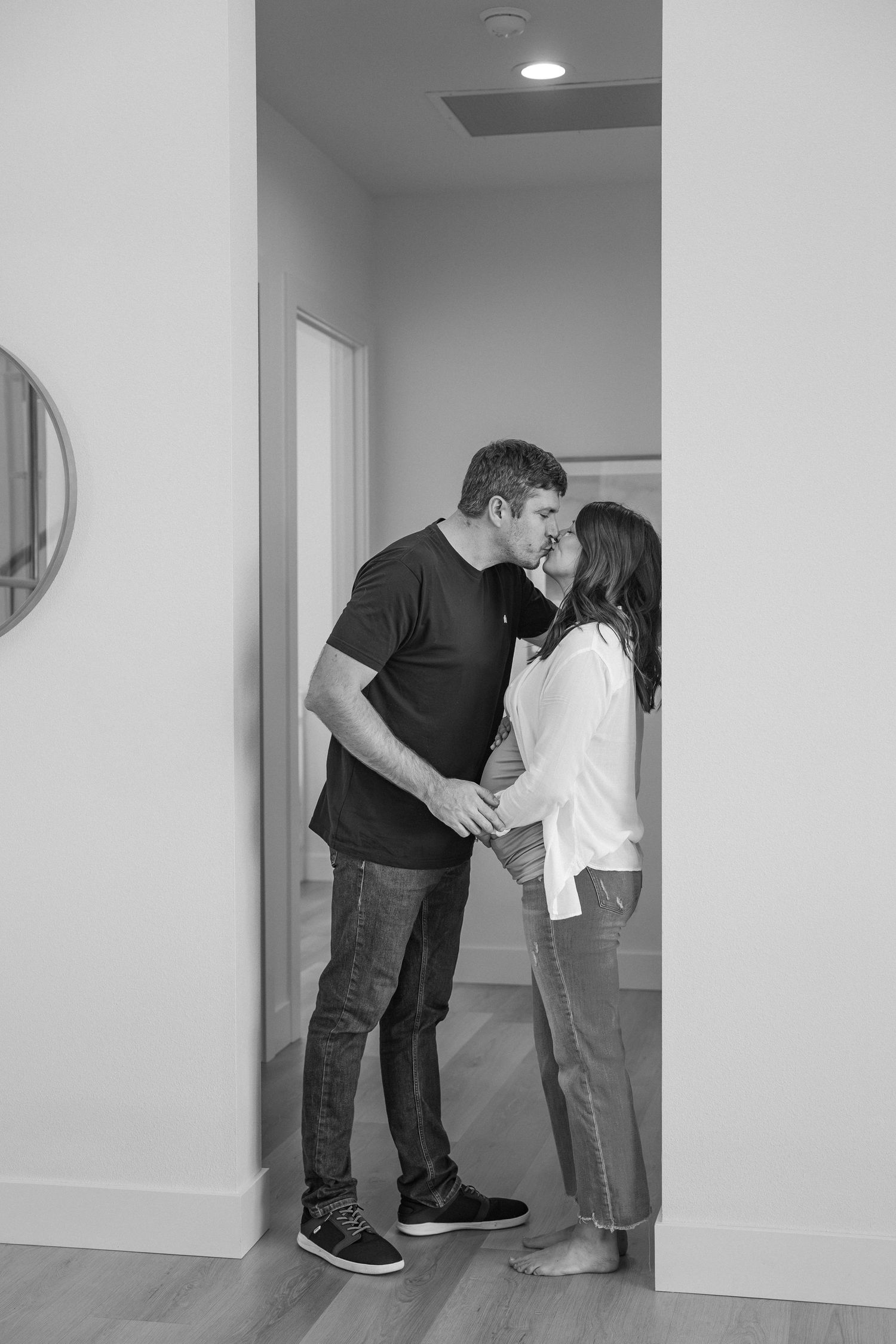 A couple shares a tender kiss in a minimalist white hallway, shown in a series of four black and white photographs.