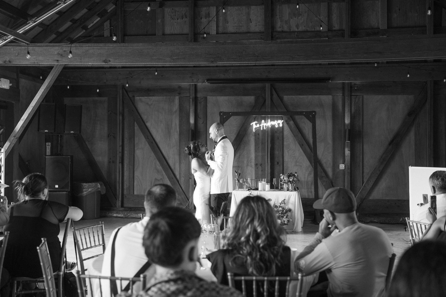 Black and white photo of a wedding celebration inside a rustic barn venue.