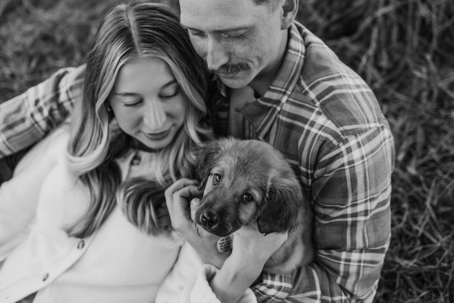 Black and white portrait series of couple cuddling with their dog outdoors.