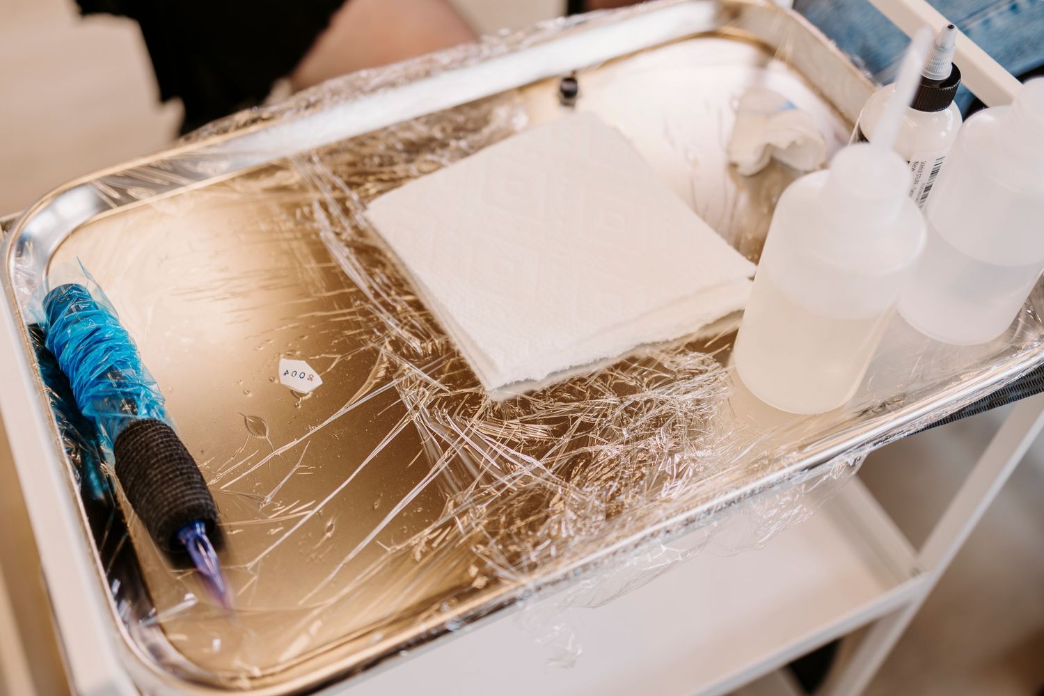 Close-up of beauty tools and supplies laid out on a metallic tray during a lash extension service.