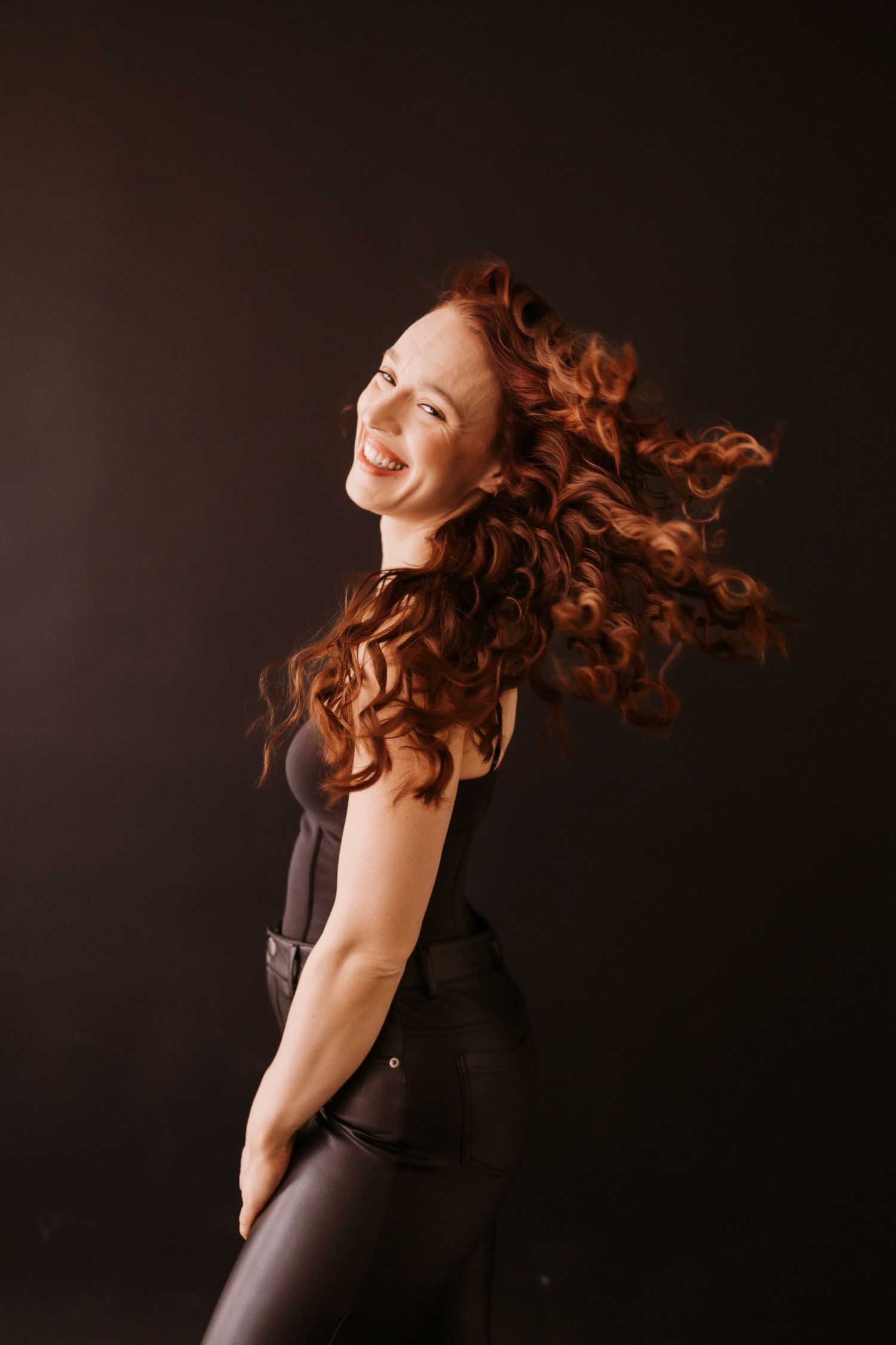 Dynamic studio portrait with flowing hair movement against dark background.