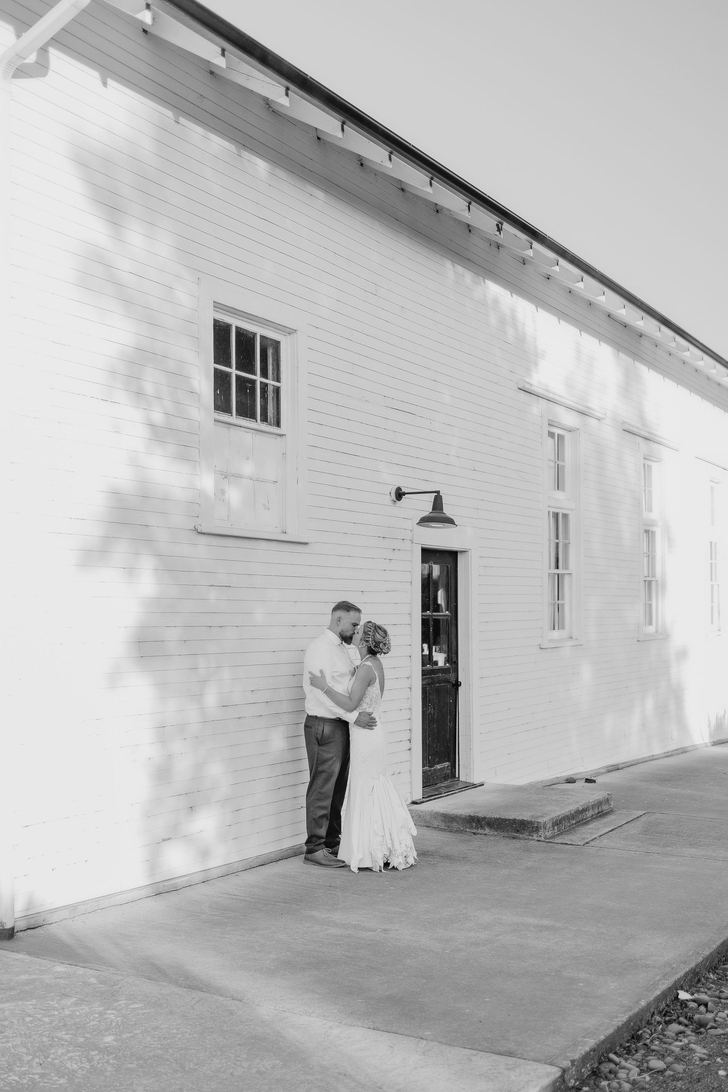 Black and white portrait of couple embracing against white building exterior.
