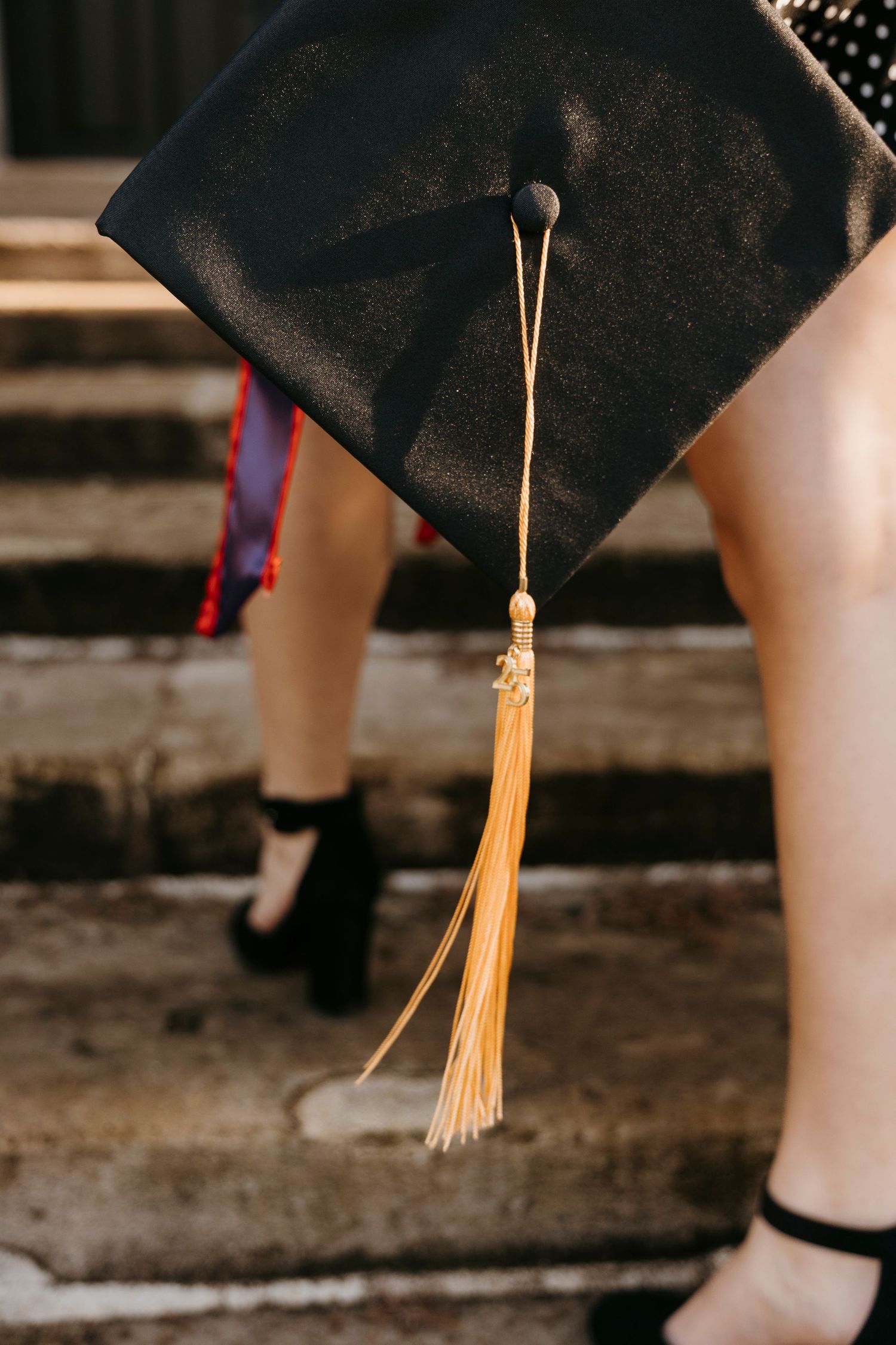 Close-up of a graduation cap with gold tassel against dark background.