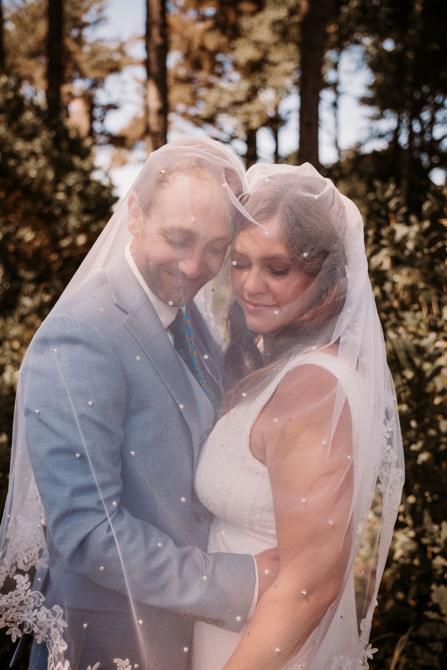 Romantic wedding couple embracing under a delicate veil in autumn sunlight.