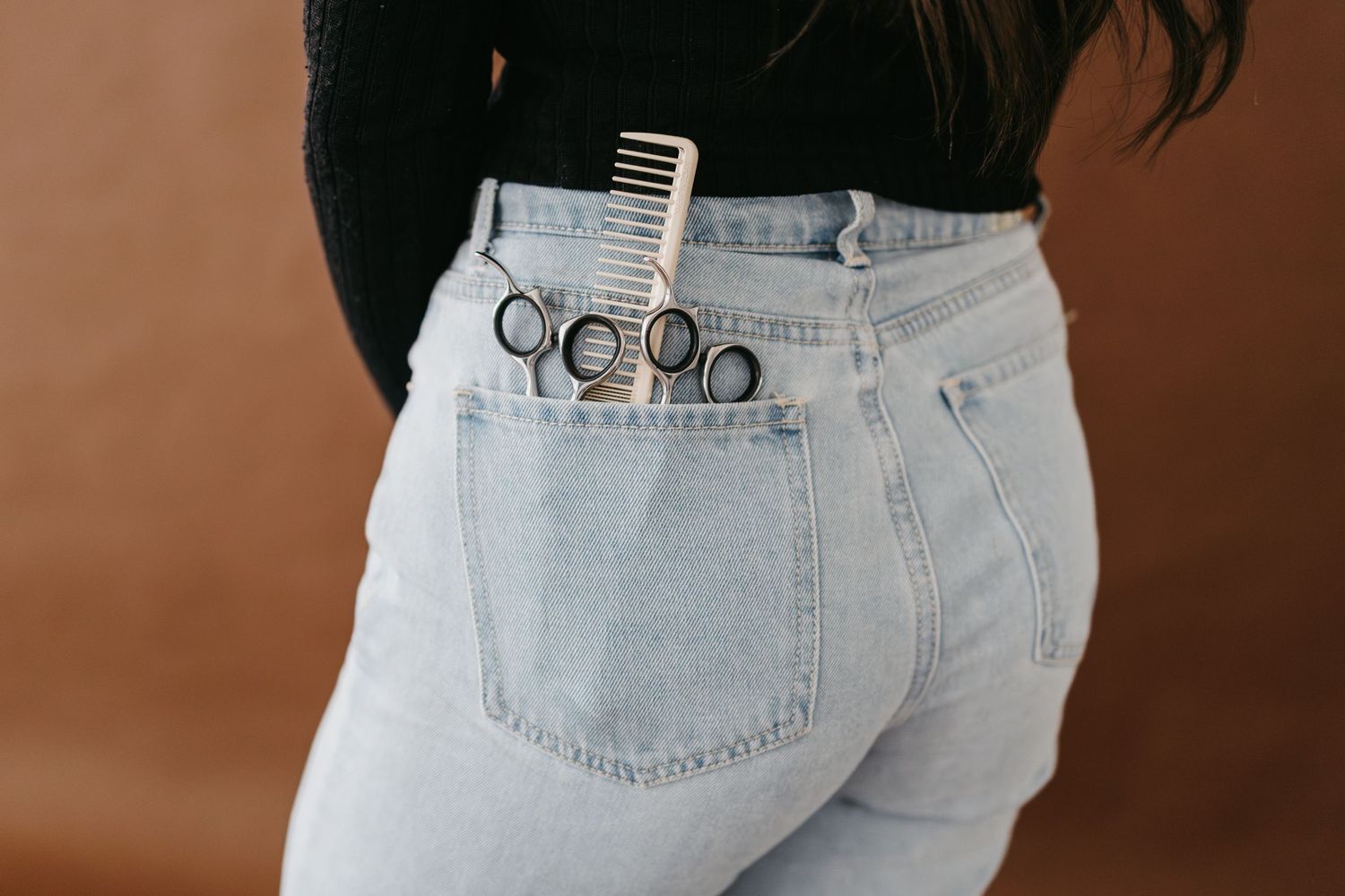 Hair styling tools and accessories arranged in back pocket of light wash denim jeans.