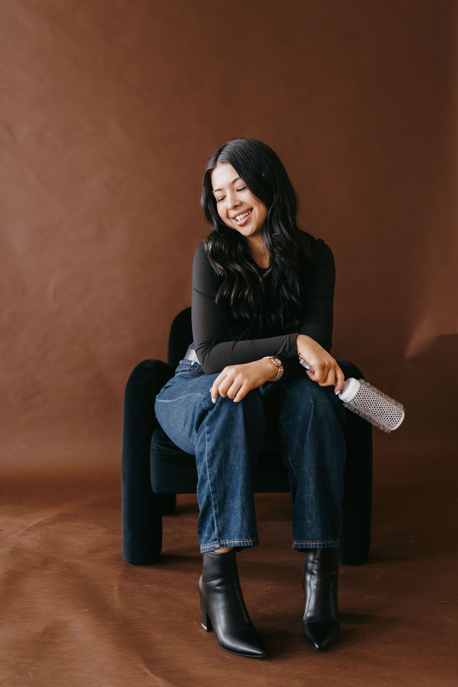 Casual styling session showing person in black top and jeans seated on brown backdrop.
