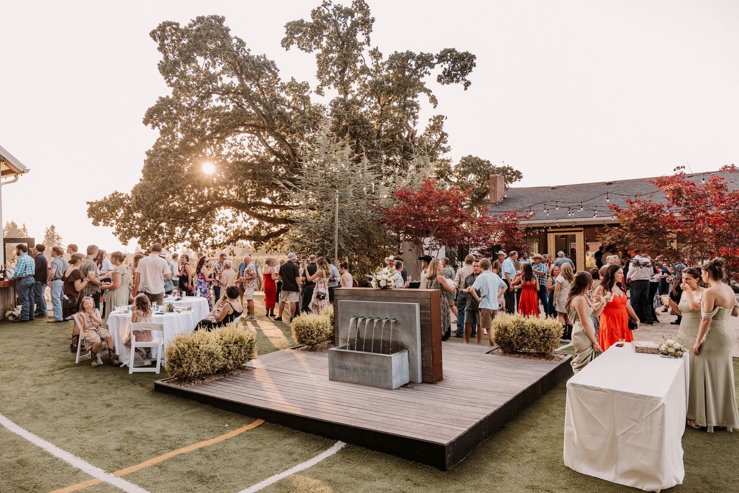Outdoor wedding ceremony setup with wooden stage and guests gathering at sunset.