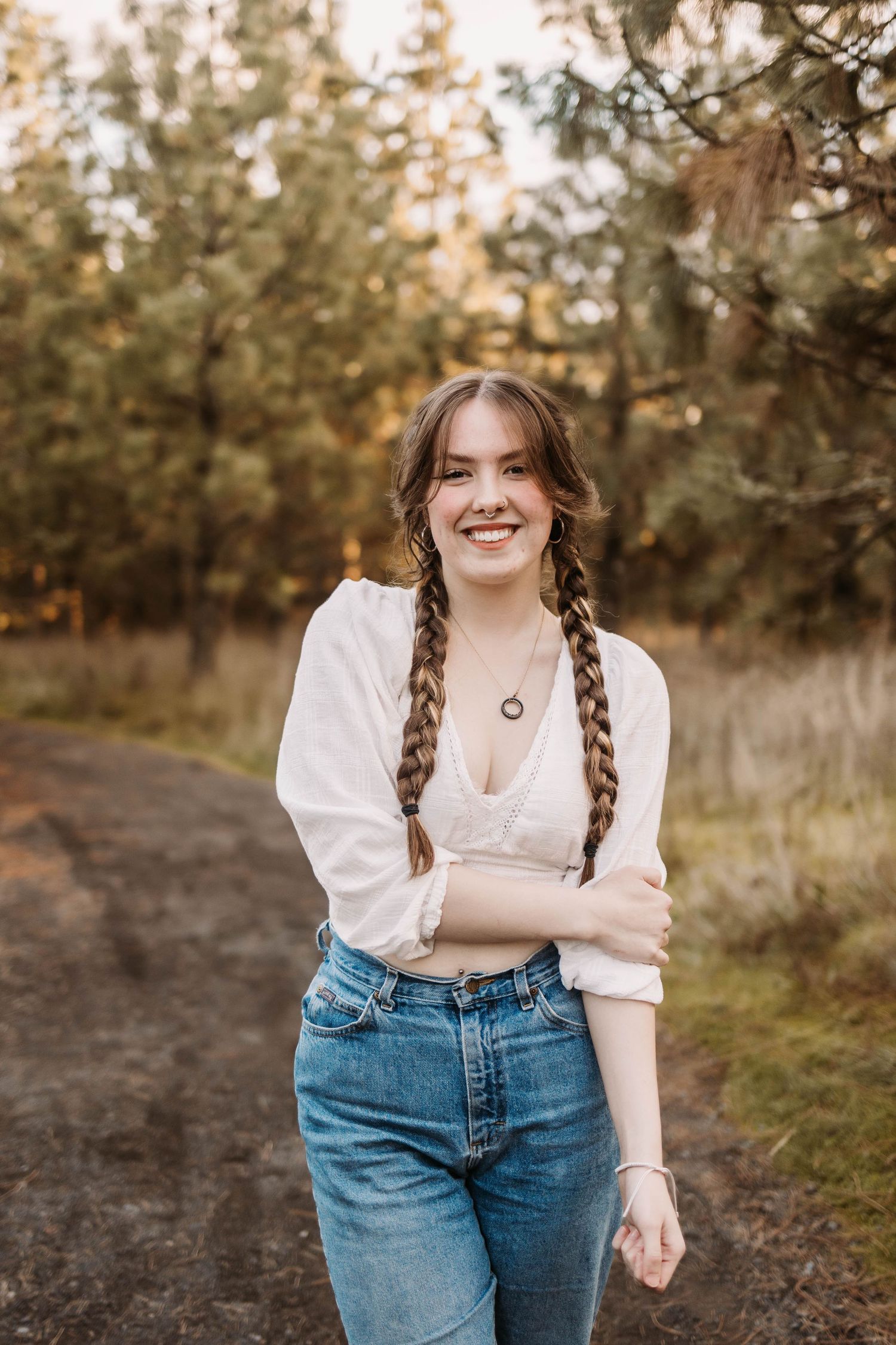 A casual outdoor portrait showing long braided hair, white blouse and jeans against a natural forest background.