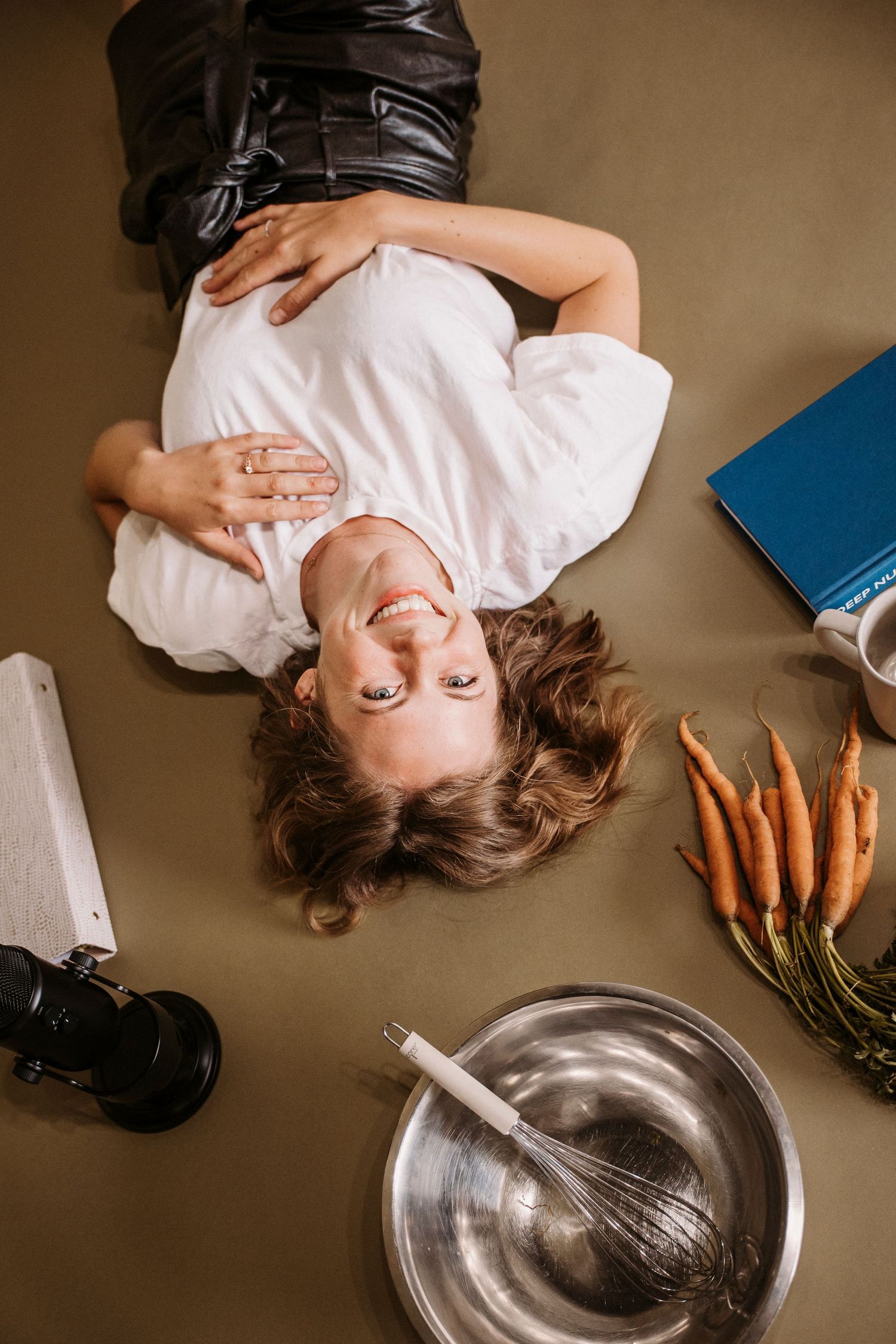 Artistic overhead shot with beauty products, carrots, and mixing bowl on brown background.