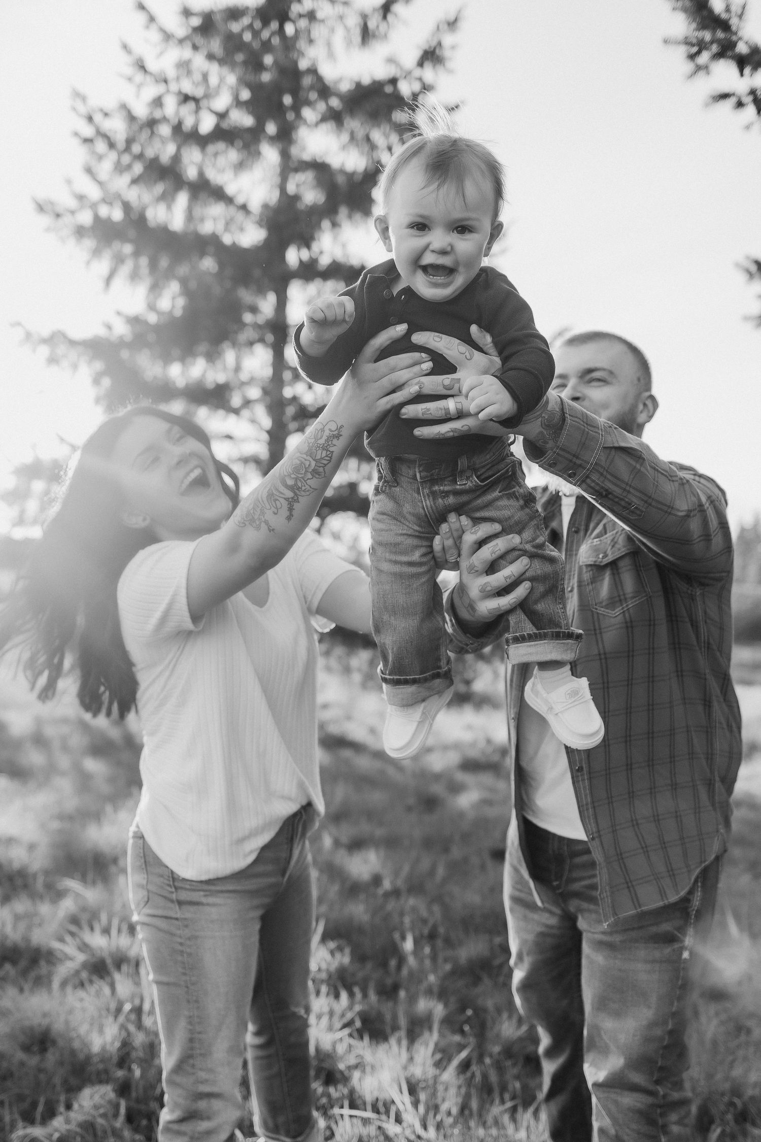 Black and white photo of parents playfully lifting child in outdoor setting.