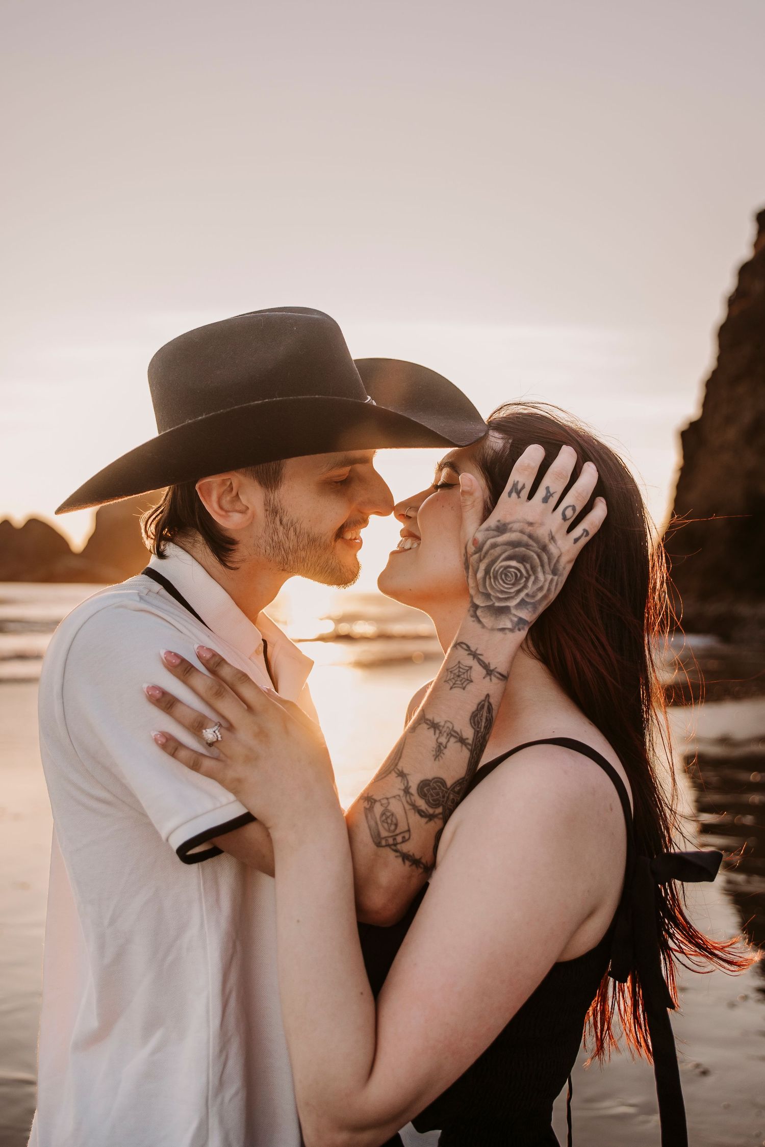 Romantic sunset beach photos showing tender moments between a couple wearing western style attire.